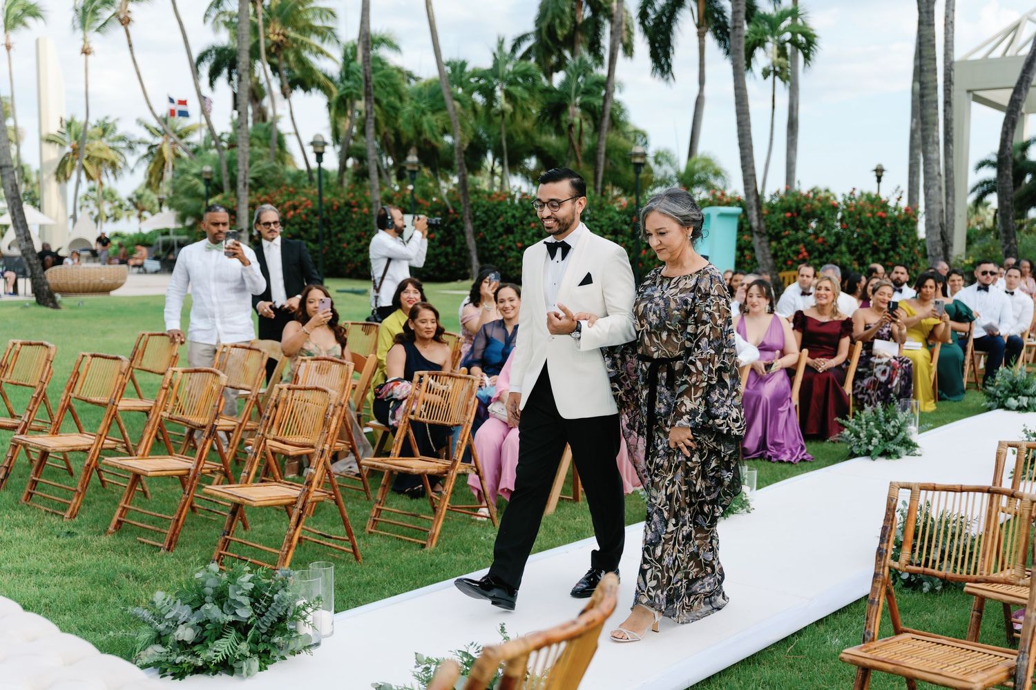 Outdoor wedding ceremony setup with wooden chairs and palm trees in a tropical garden setting.