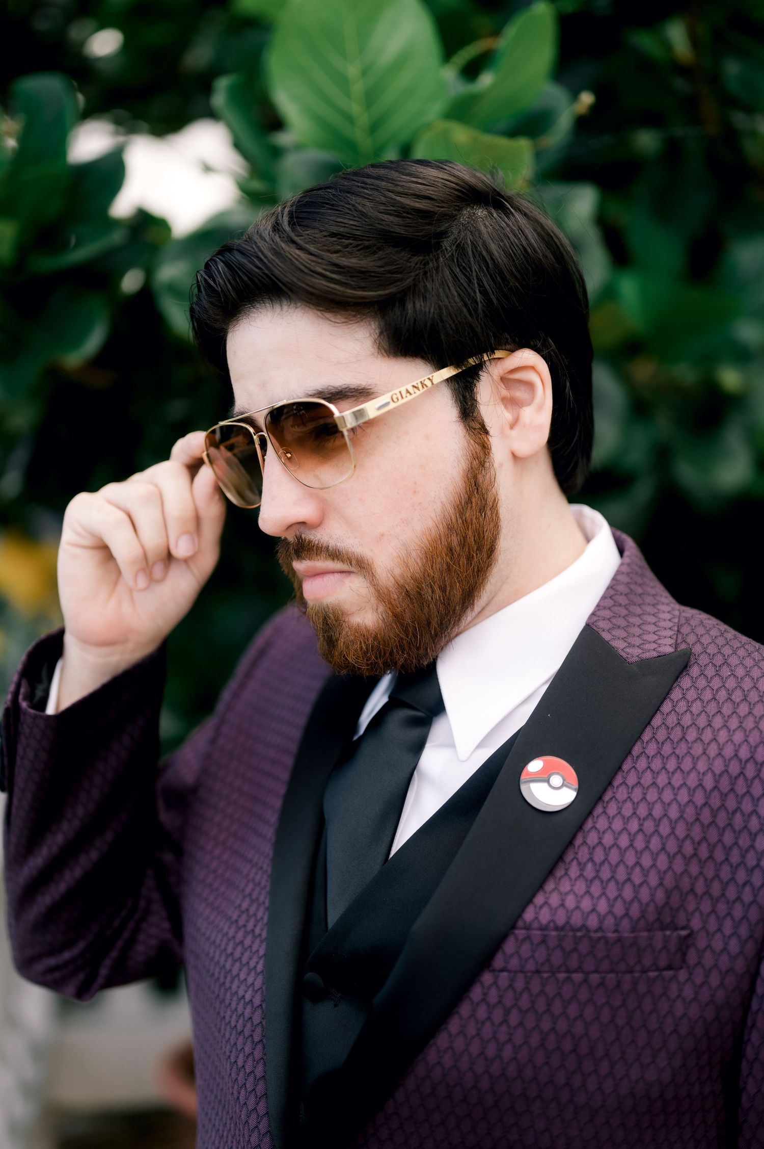 Stylish man in purple polka dot blazer and sunglasses poses in a series of photos against green foliage background.