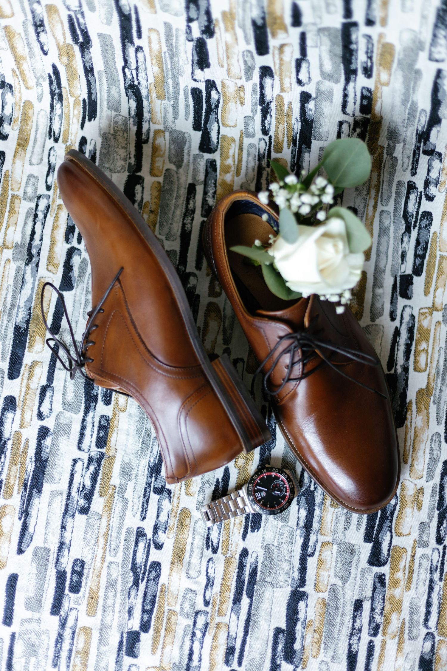 Brown leather dress shoes arranged in a row against a patterned background with delicate white flowers.