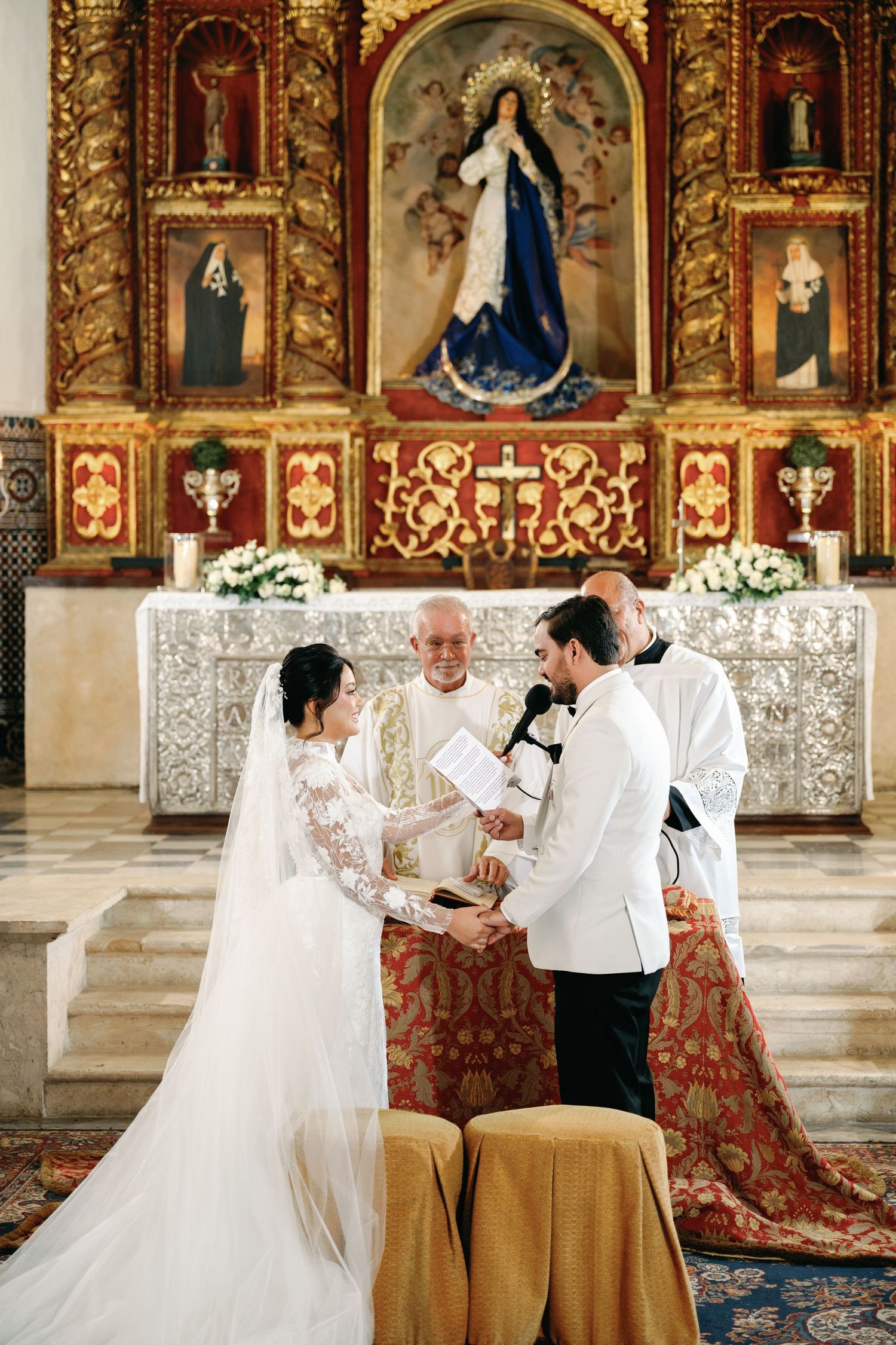 Traditional Catholic wedding ceremony taking place in an ornate church with gilded altarpiece and religious artwork.
