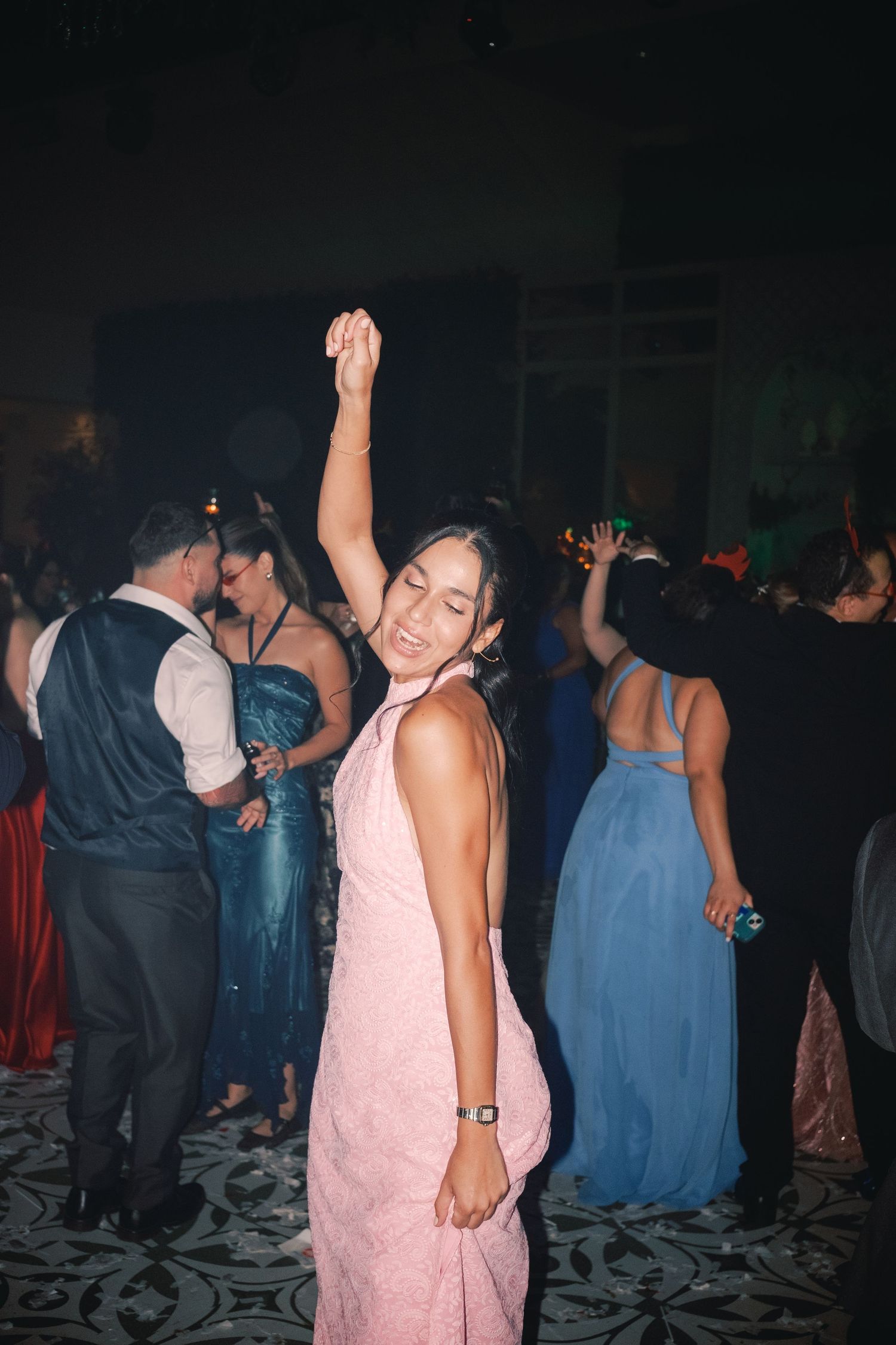 Woman in pink dress dances with raised arm on crowded dance floor at formal event.