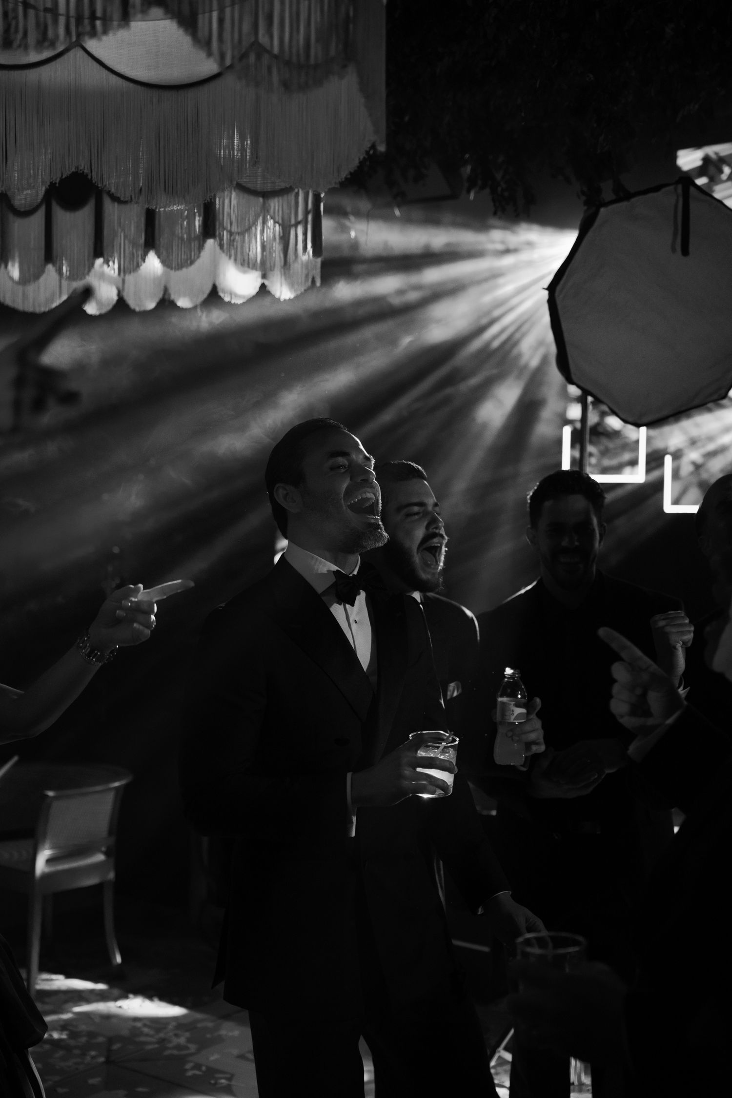 Silhouettes of guests enjoying drinks and conversation in a dimly lit venue with dramatic light beams.