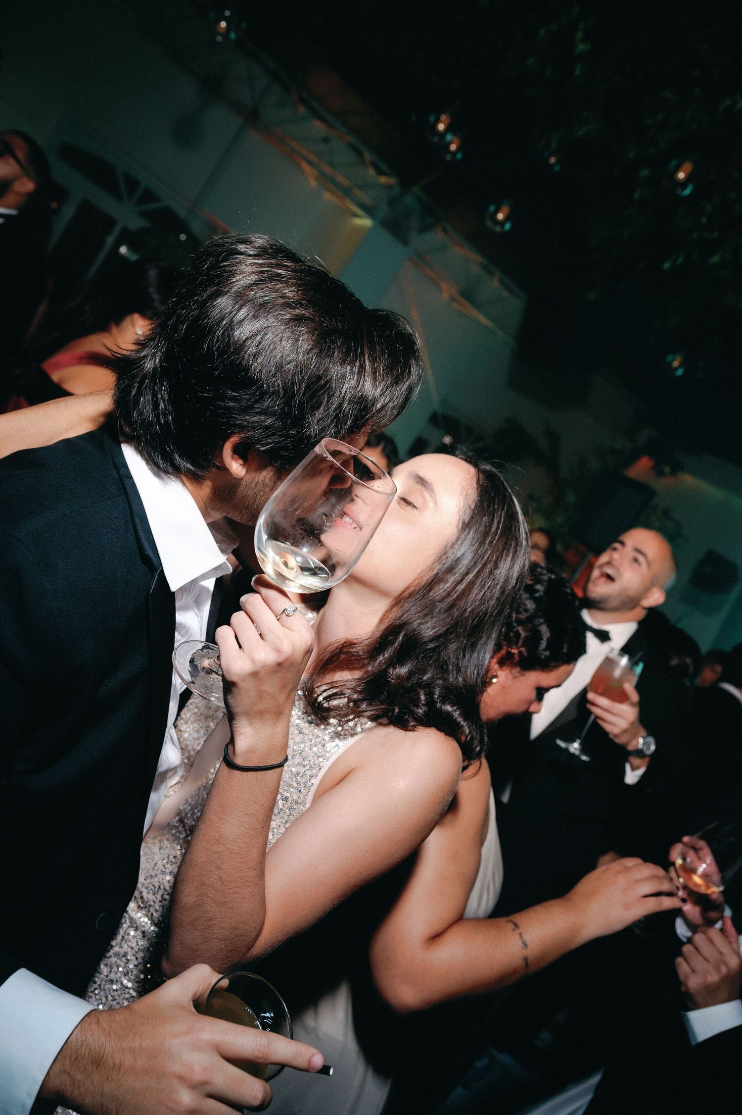 A couple shares a romantic kiss on the dance floor during a wedding celebration in a dimly lit venue.
