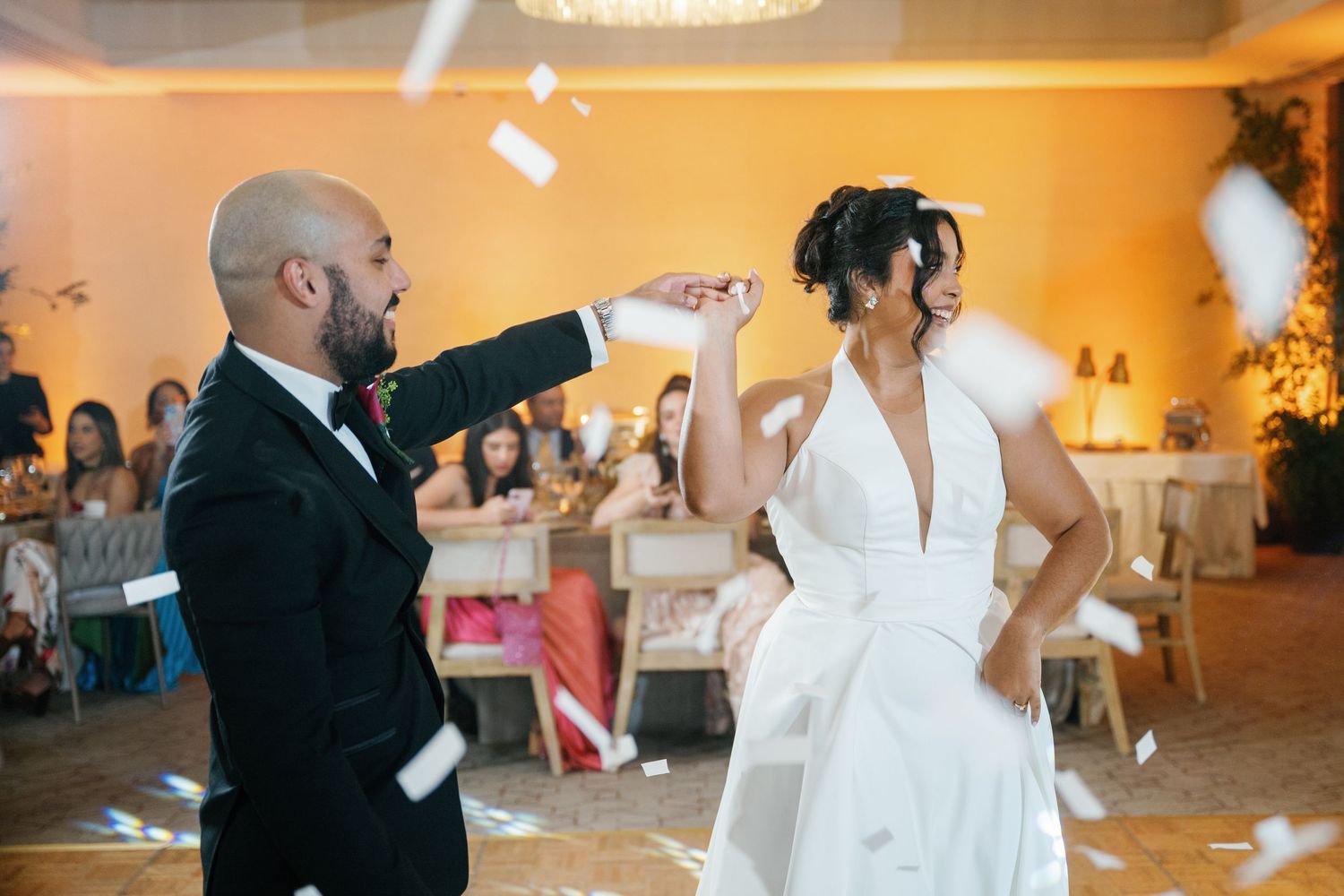 Dancers perform energetic dance moves at a wedding reception in a warmly lit ballroom.