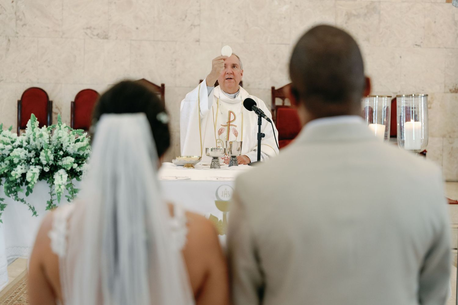 A couple stands at the altar during their wedding ceremony with floral decorations in the background.