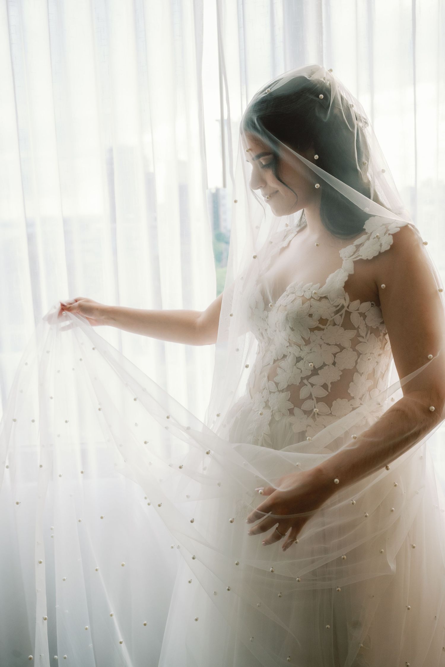 Ethereal silhouette of a bride in a lace wedding dress against sheer white curtains in natural light.