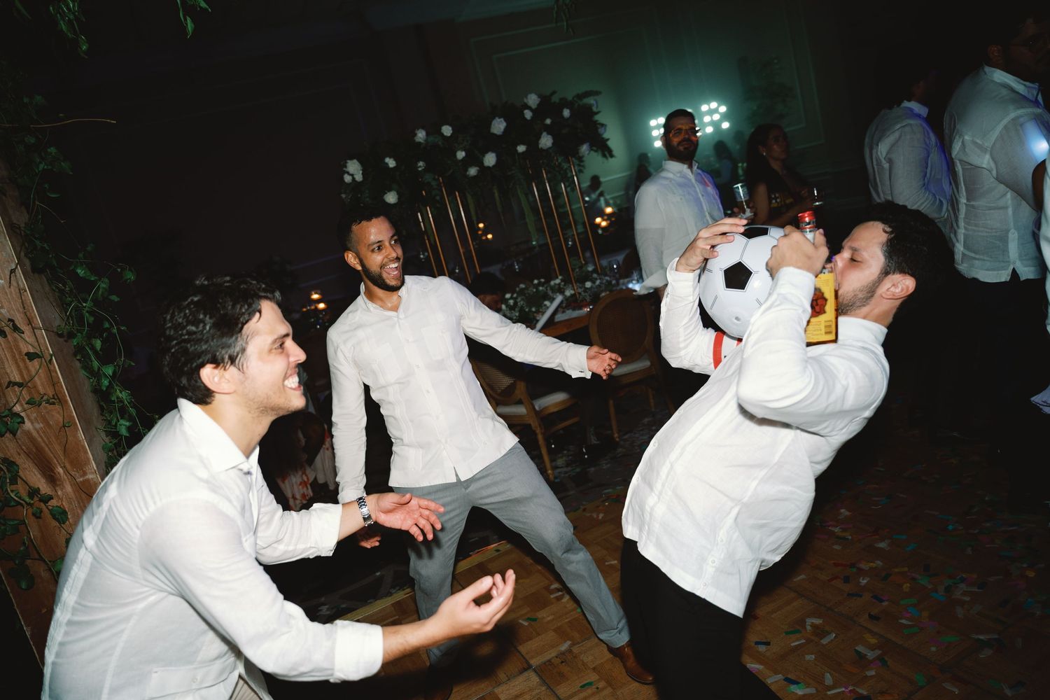 A lively nighttime celebration shows partygoers in white shirts dancing and socializing in a dark outdoor setting.