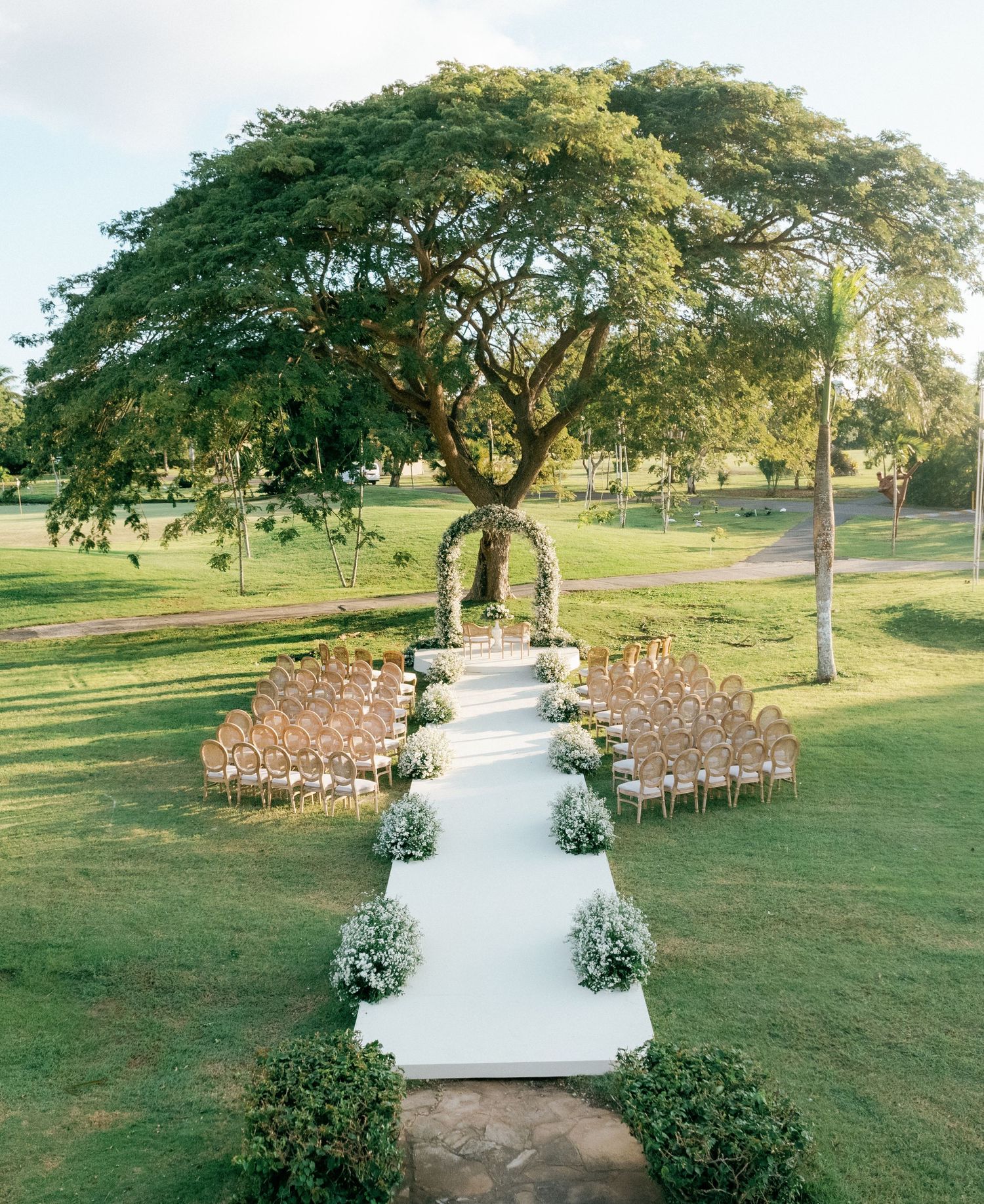 Outdoor wedding ceremony setup with white aisle runner and wooden chairs on a grassy hillside.