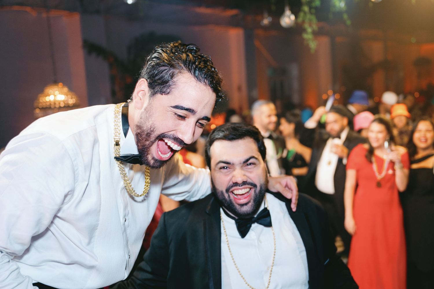 Wedding guests laugh and dance together during a joyful celebration on the dance floor at an evening reception.