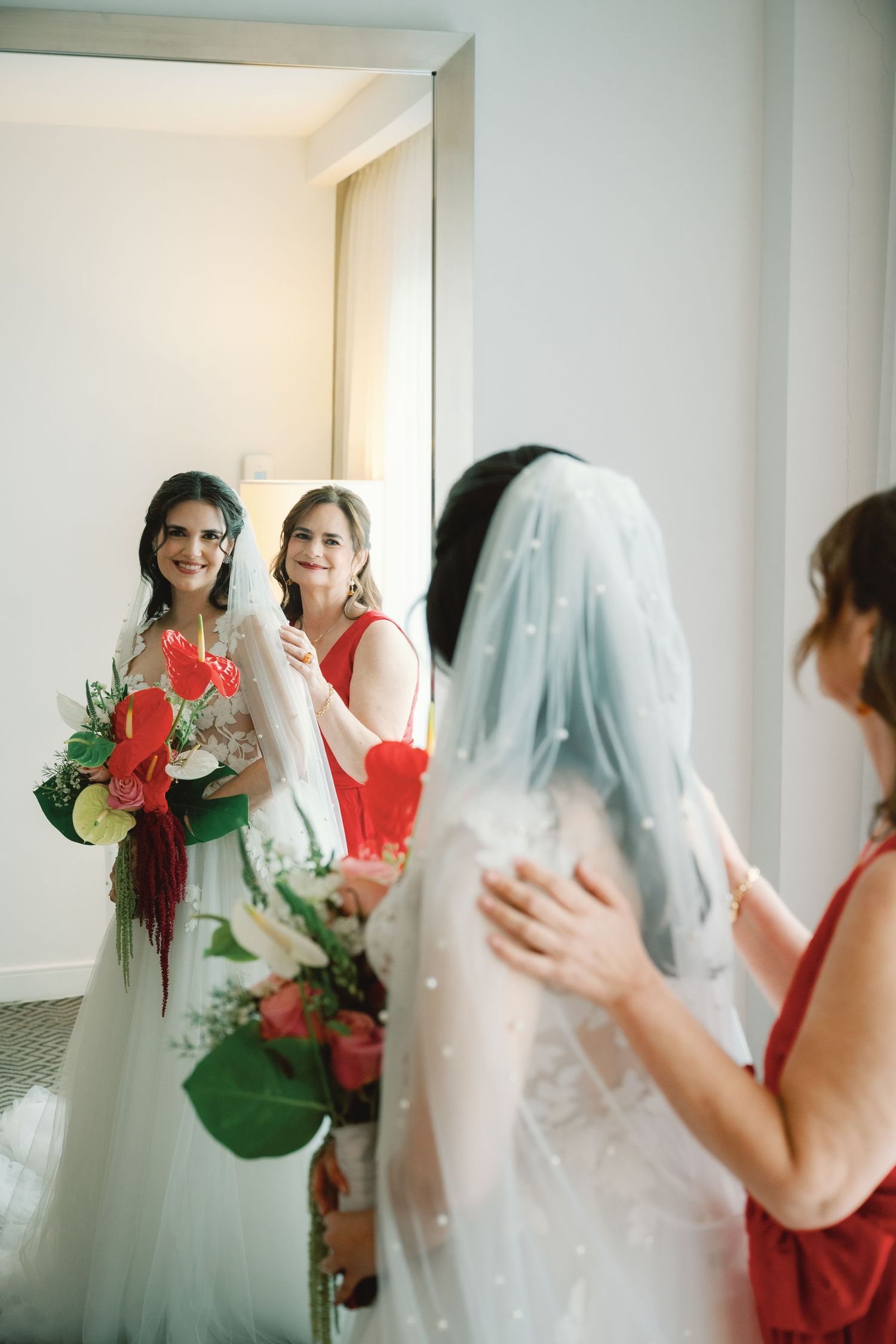 Bridesmaids in coral dresses help prepare the bride in her wedding gown and veil during pre-ceremony preparations.