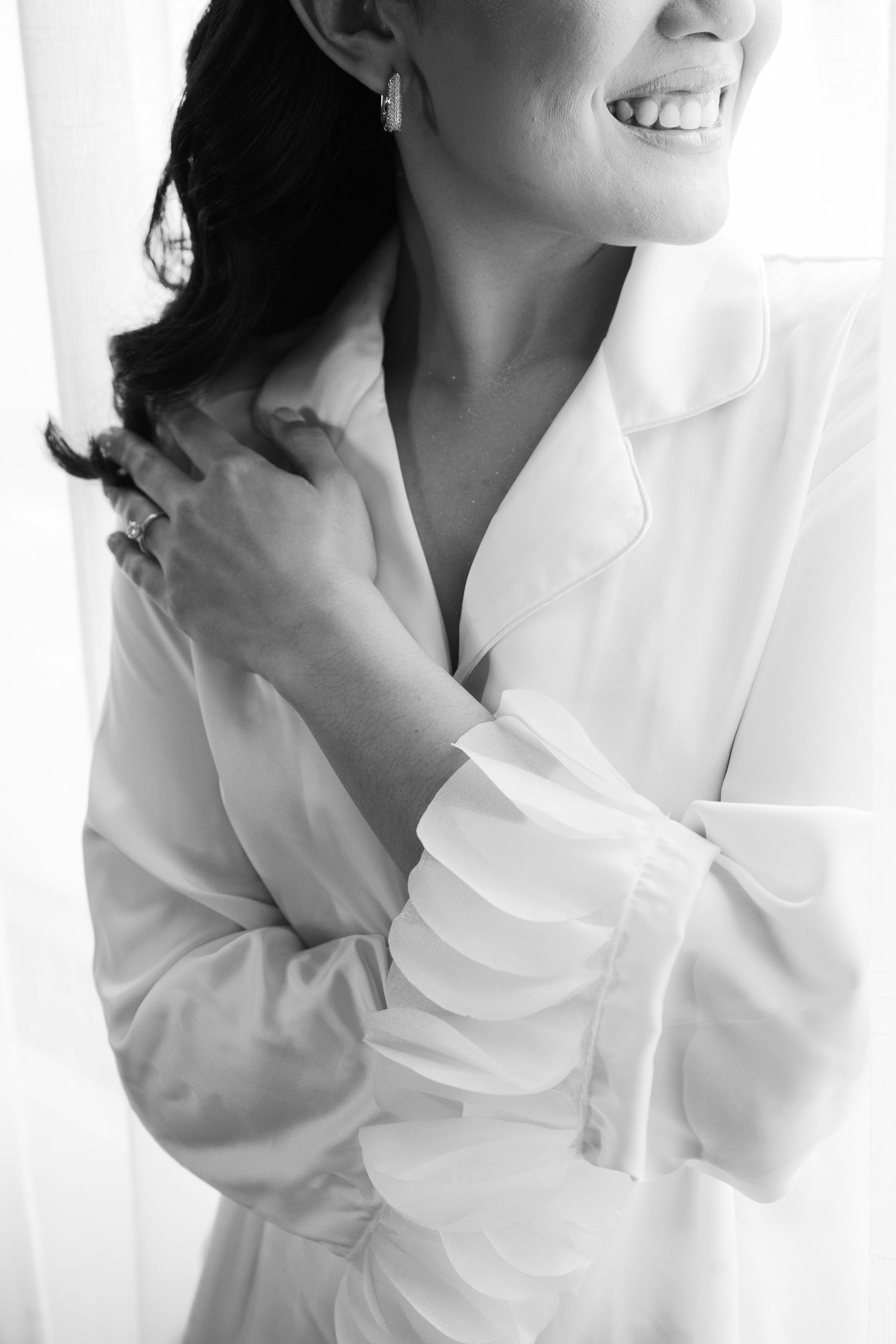 Black and white portrait of someone in a white button-down shirt smiling and touching their shoulder.