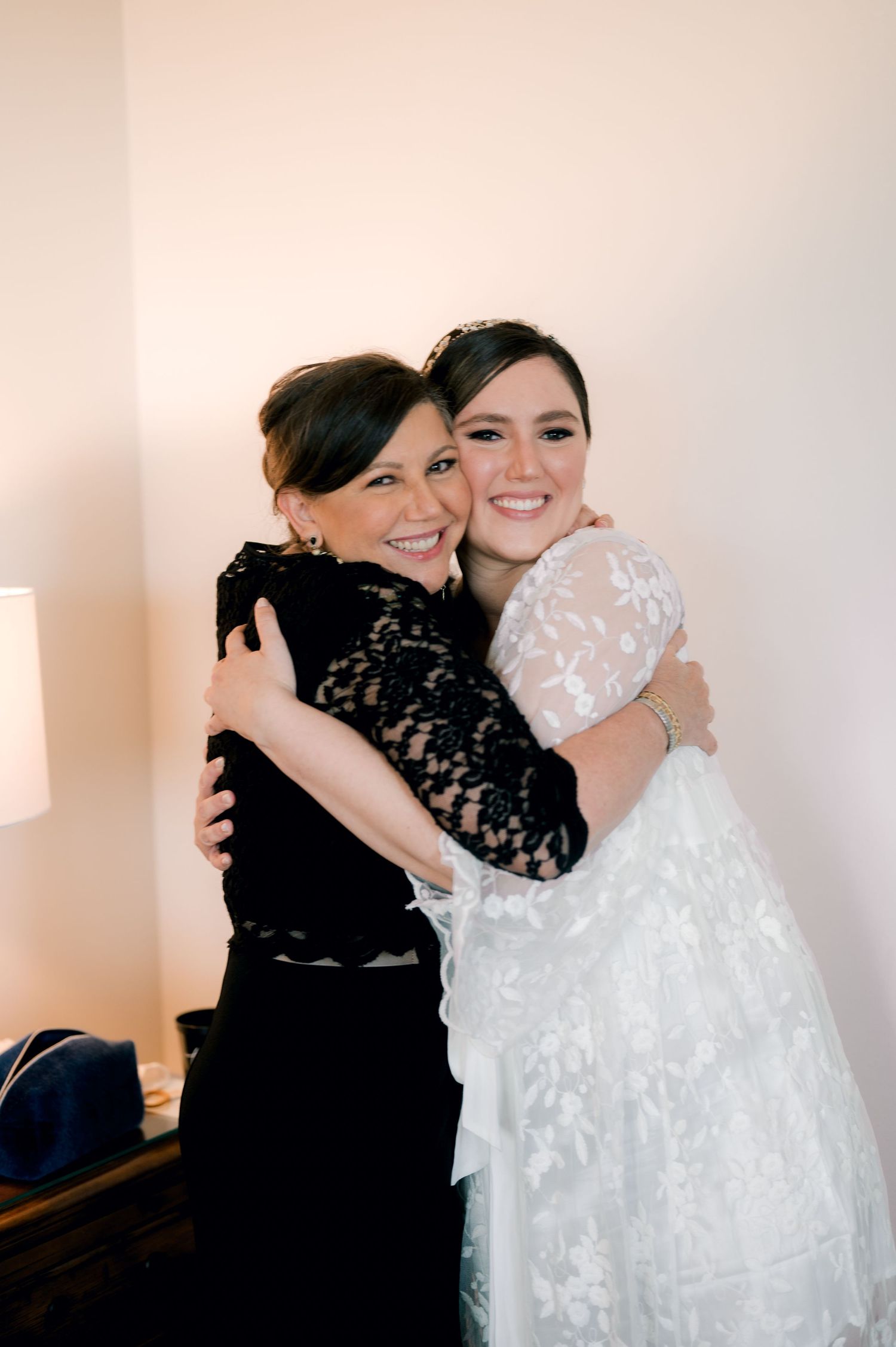 Two people share emotional embraces in a series of photos, one wearing a white lace wedding dress and the other in black.