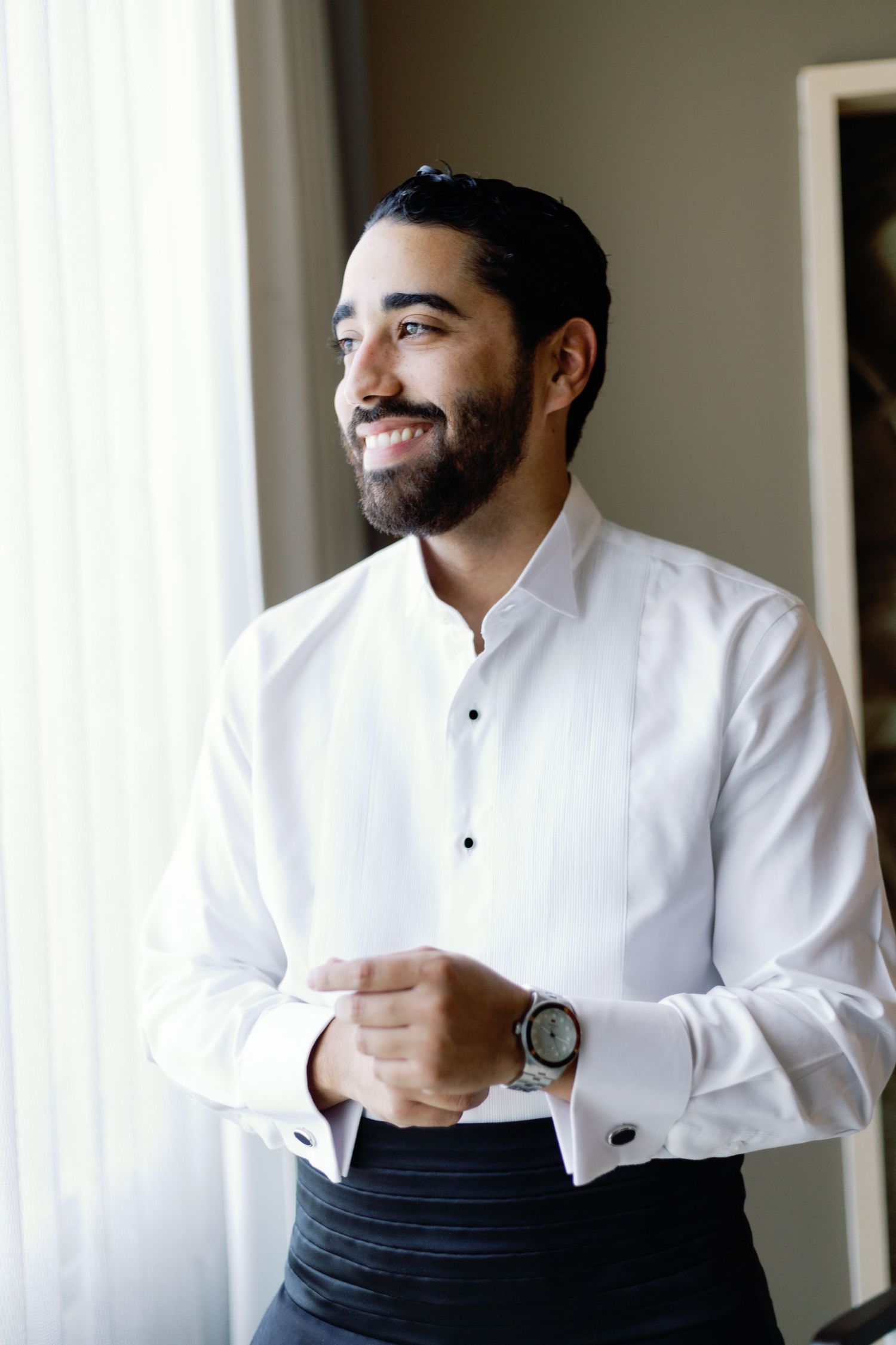A person in a crisp white dress shirt adjusts their cuffs while getting ready for a formal occasion.