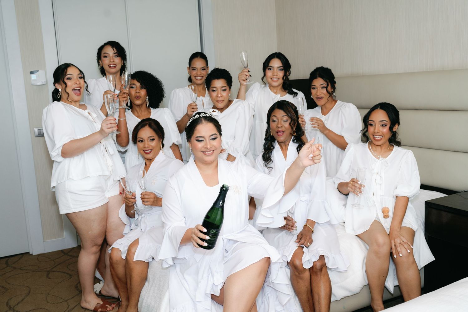 A group in white robes and sleepwear celebrates together while holding a champagne bottle.