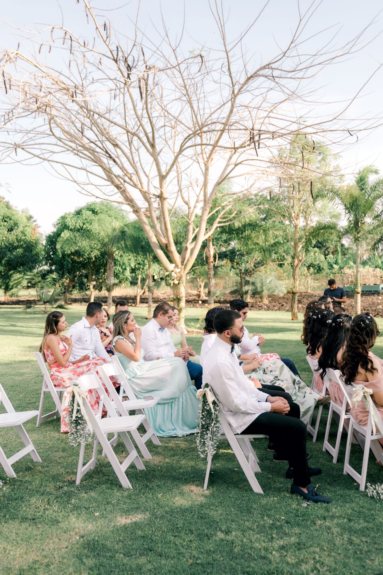 Wedding guests seated in white chairs on a lawn play a fun game during an outdoor reception ceremony.