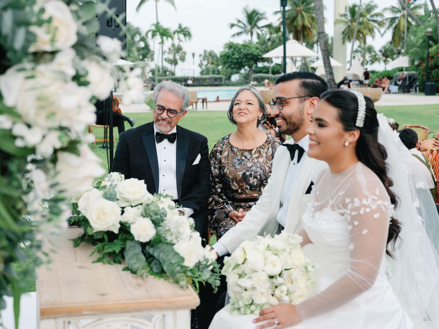Tropical beach wedding ceremony with palm trees and white decor along the oceanfront.
