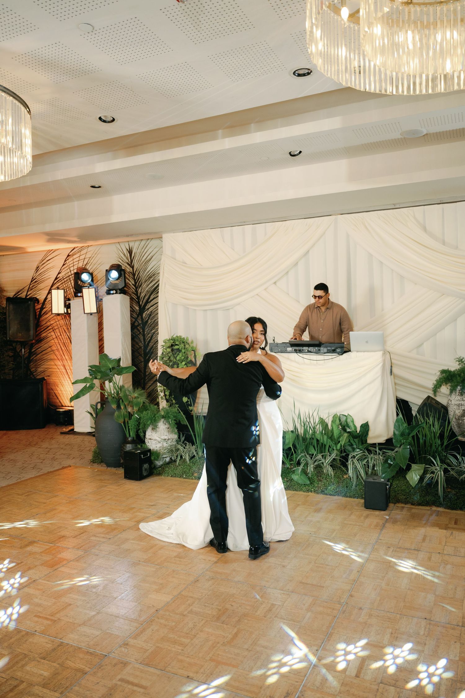 Wedding reception venue with draped white walls, chandeliers, and scattered petals on tiled floor.