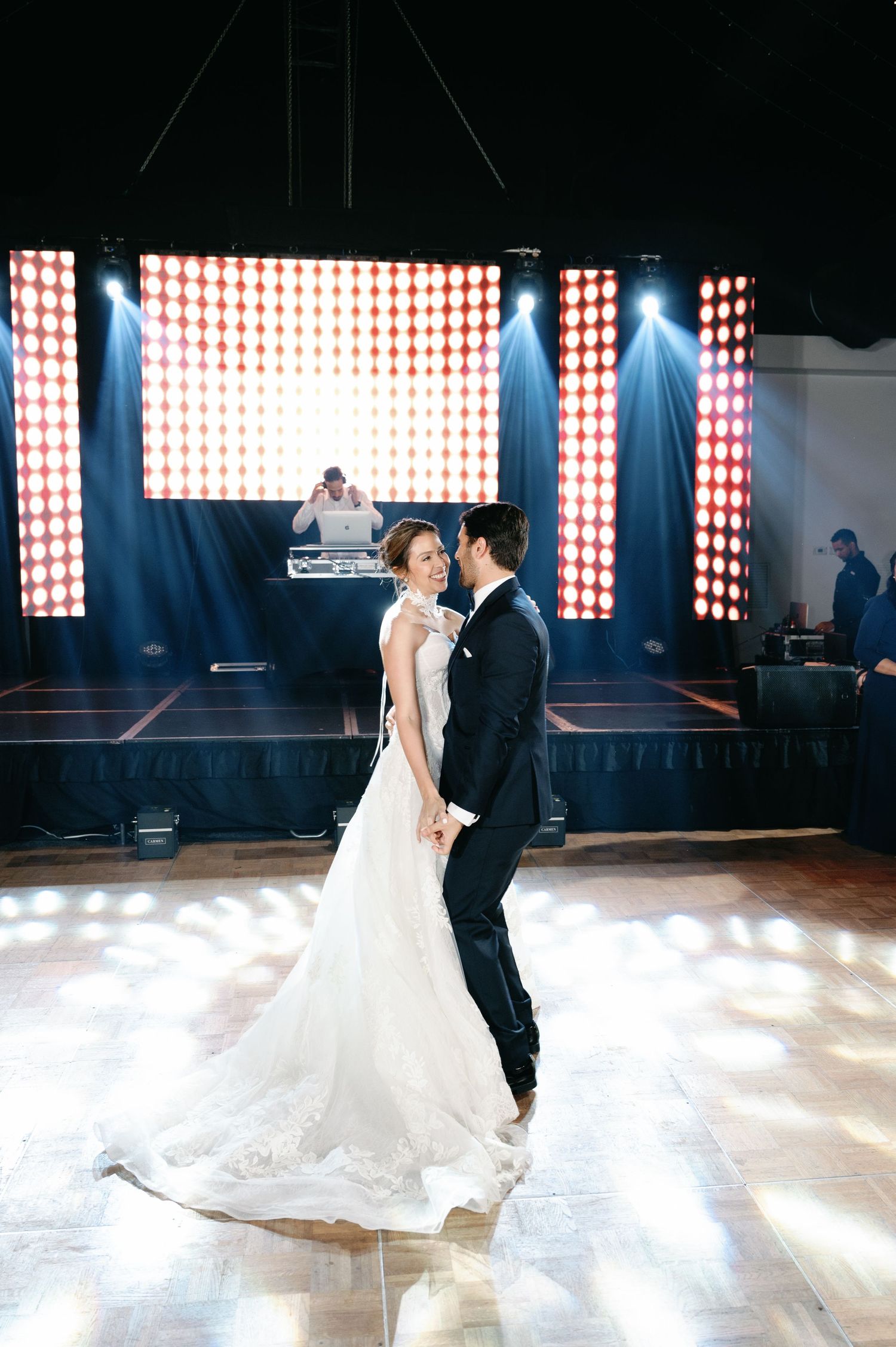 Couple dancing in an elegant venue with dramatic lighting and red checkered backdrop.