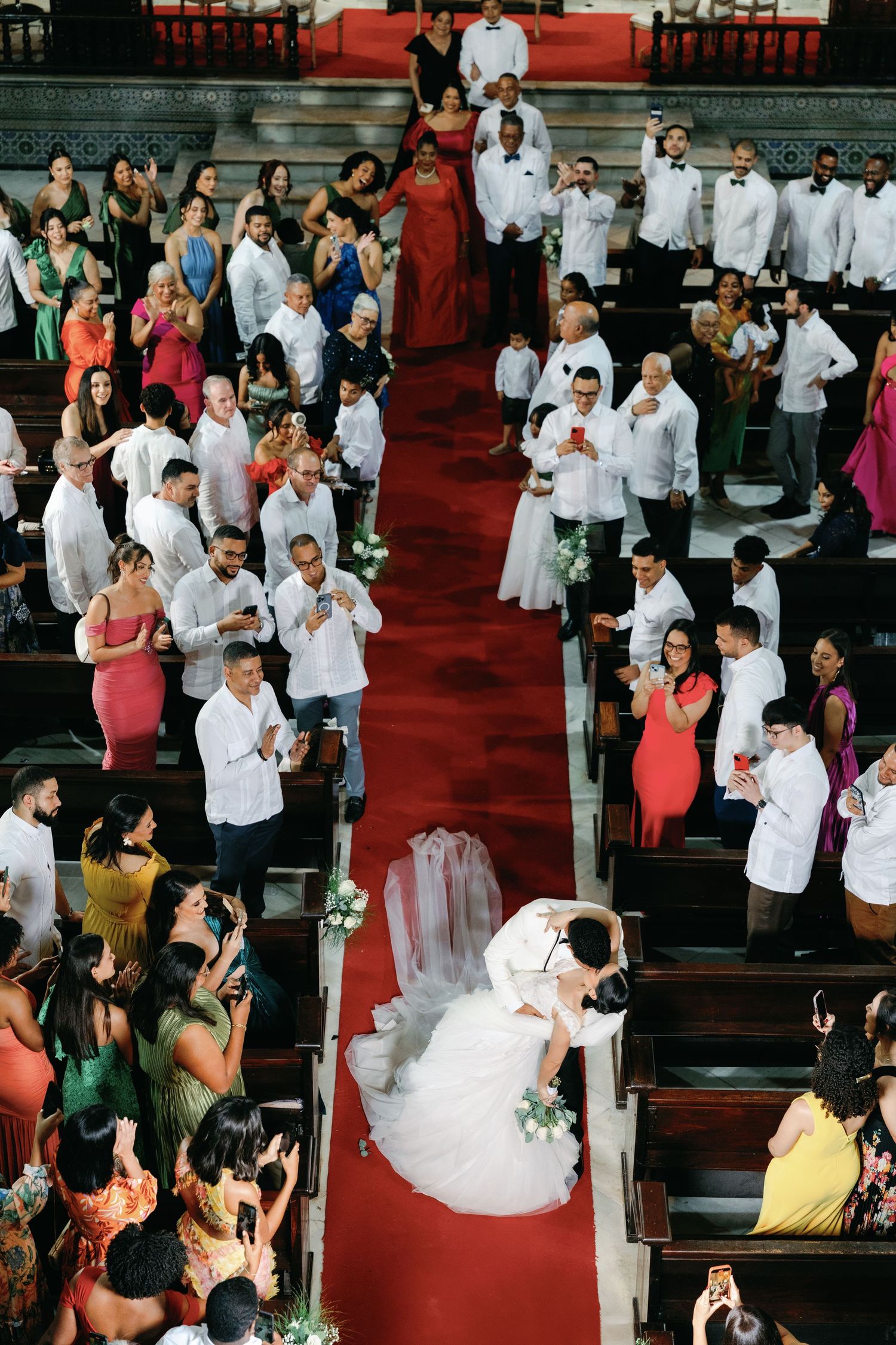 Wedding ceremony procession in church with guests seated along red-carpeted aisle.