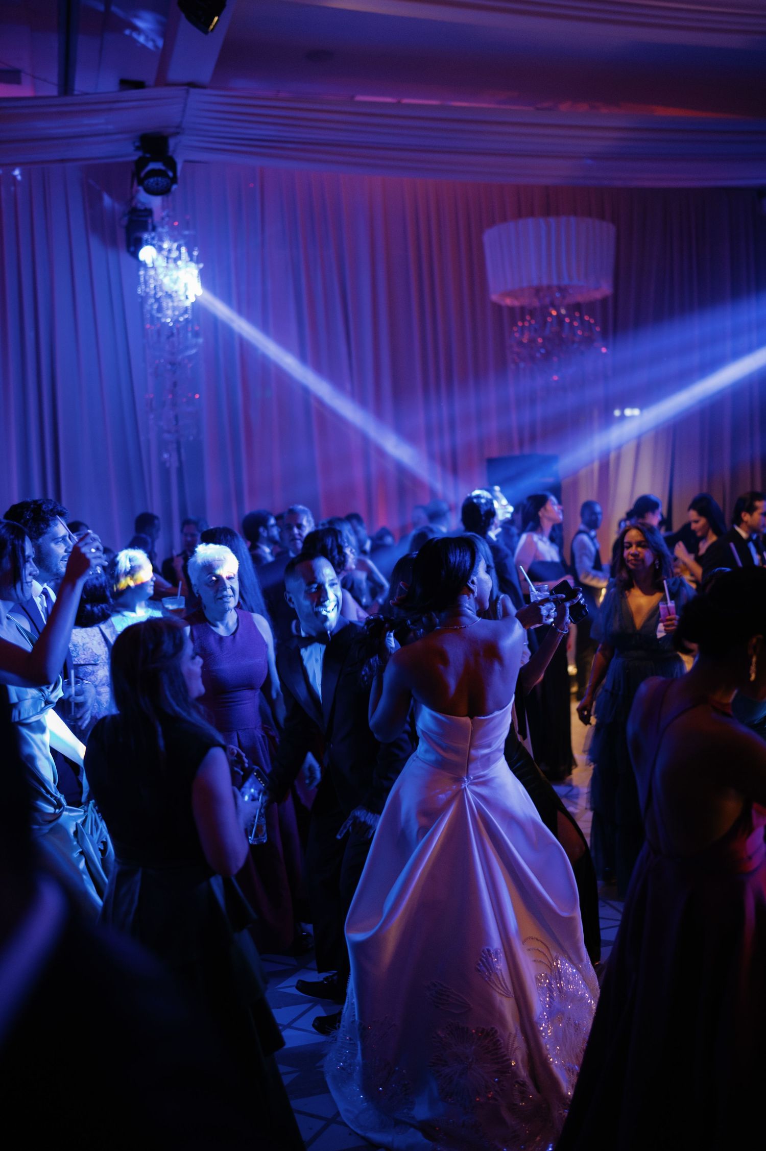 Wedding reception dance floor with purple lighting and guests celebrating under dramatic spotlights.