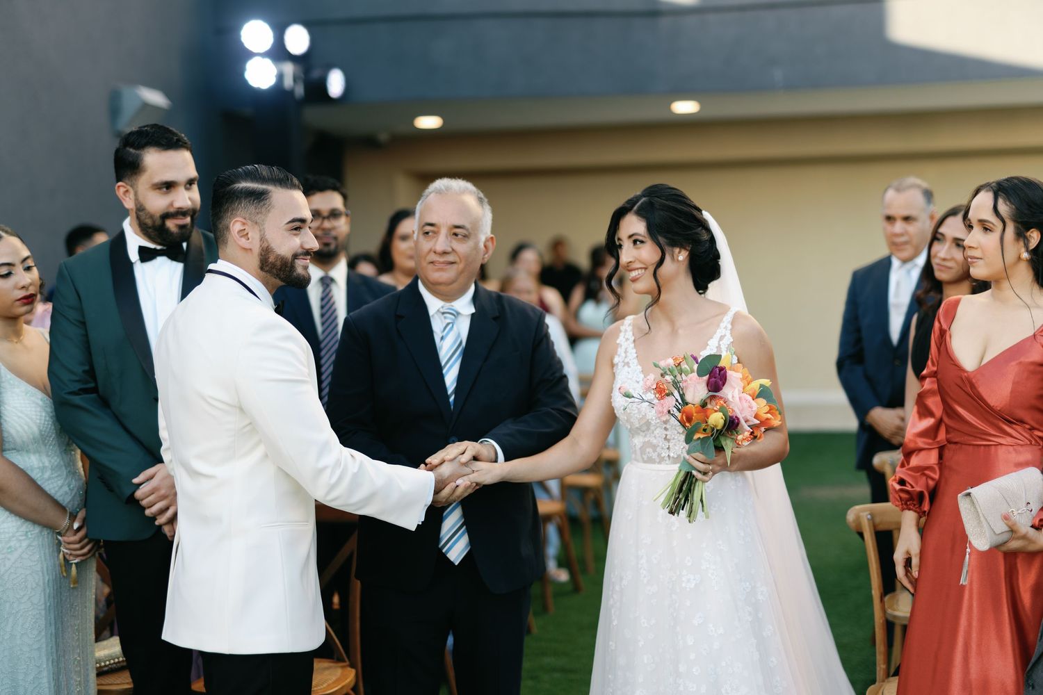 A group of wedding guests dancing and celebrating together at an indoor reception venue with warm lighting.