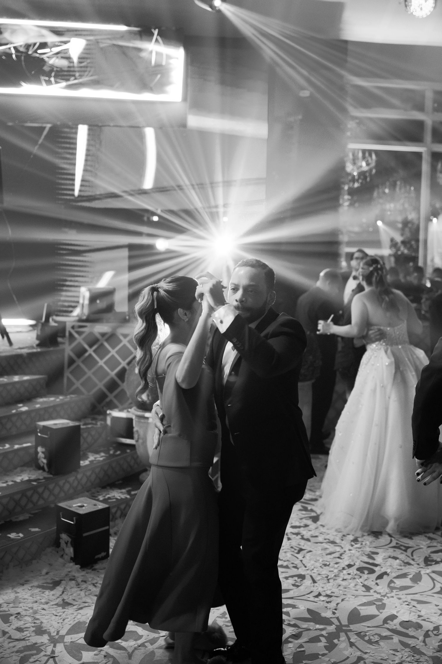 Black and white photo showing formal dresses and suits hanging on display in a room with dramatic lighting effects.