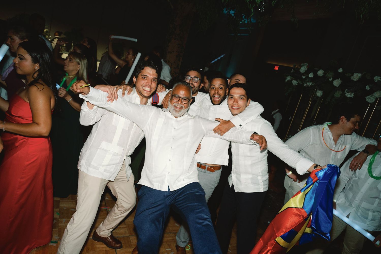 People dancing and celebrating at a lively party wearing white and dark colored outfits on a dance floor.
