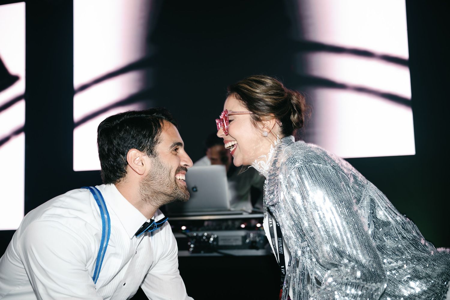 Two guests share a joyful moment at a party under dramatic lighting.