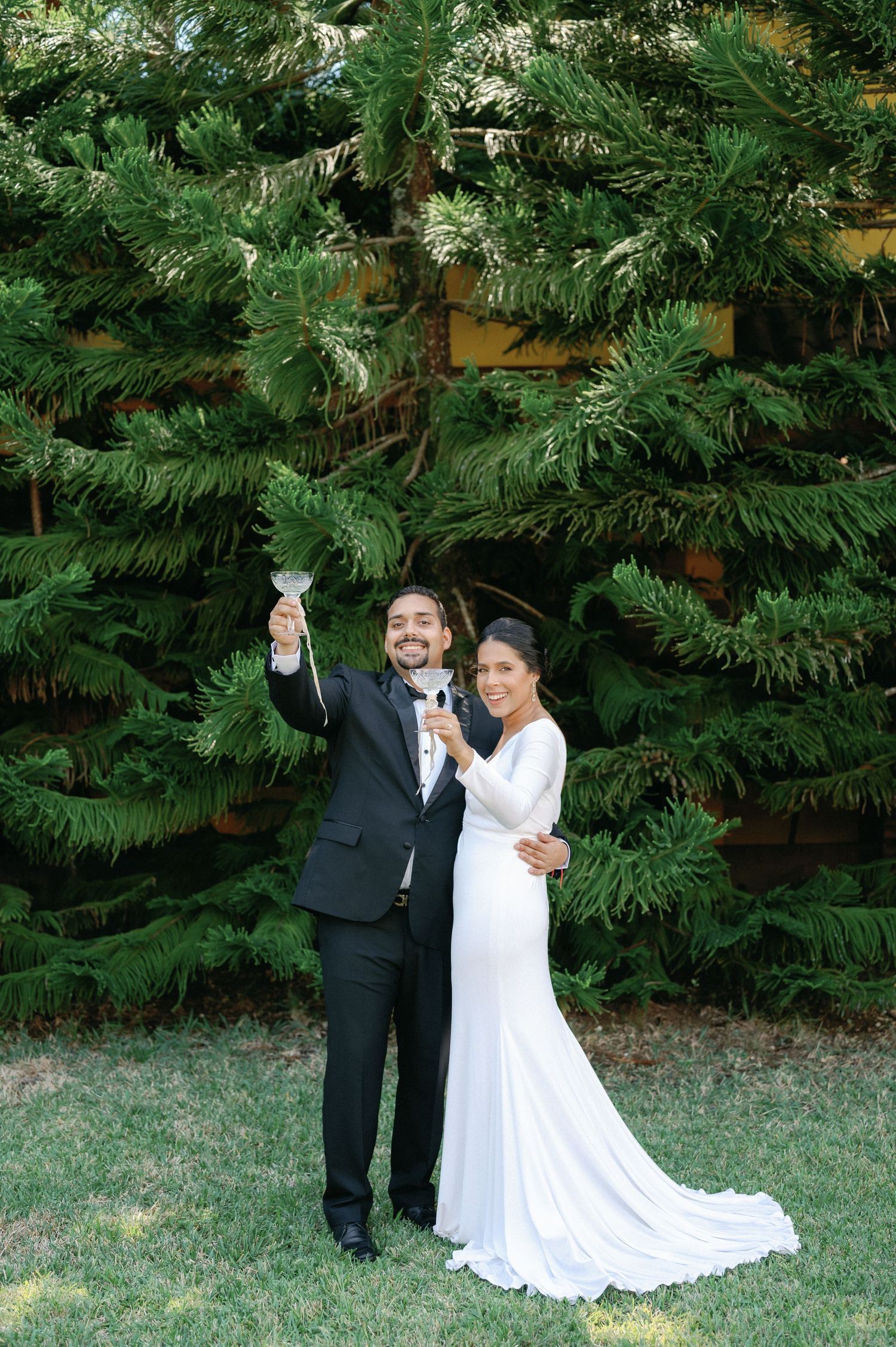 A couple in wedding attire shares intimate moments together in a lush garden setting with green foliage backdrop.
