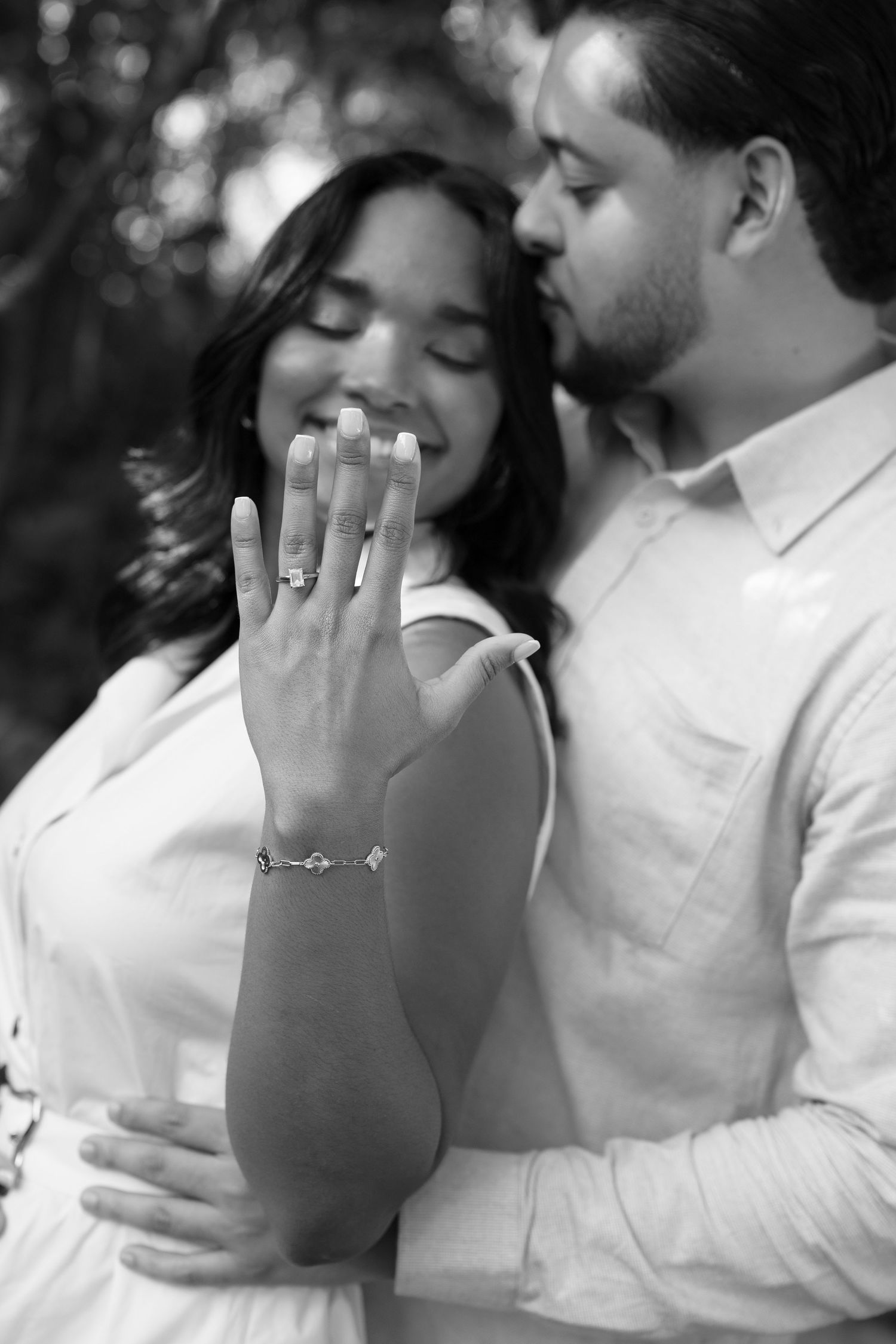 A romantic black and white engagement photo showing a close embrace and sparkling diamond ring display.