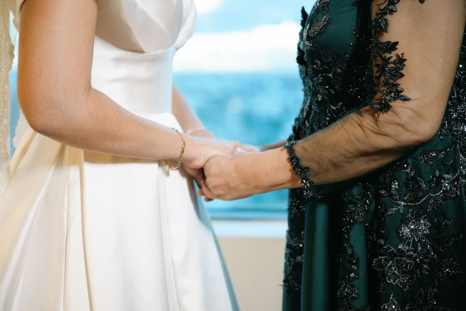 A couple embraces during an outdoor wedding ceremony with a scenic waterfront backdrop and lush greenery.