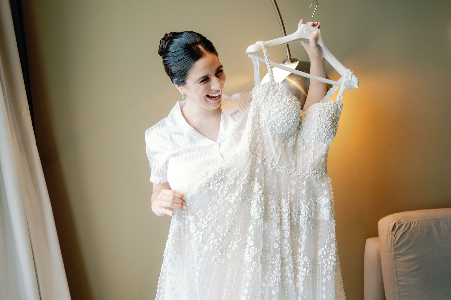 A wedding dress hangs elegantly against a neutral wall while being photographed during pre-ceremony preparations.