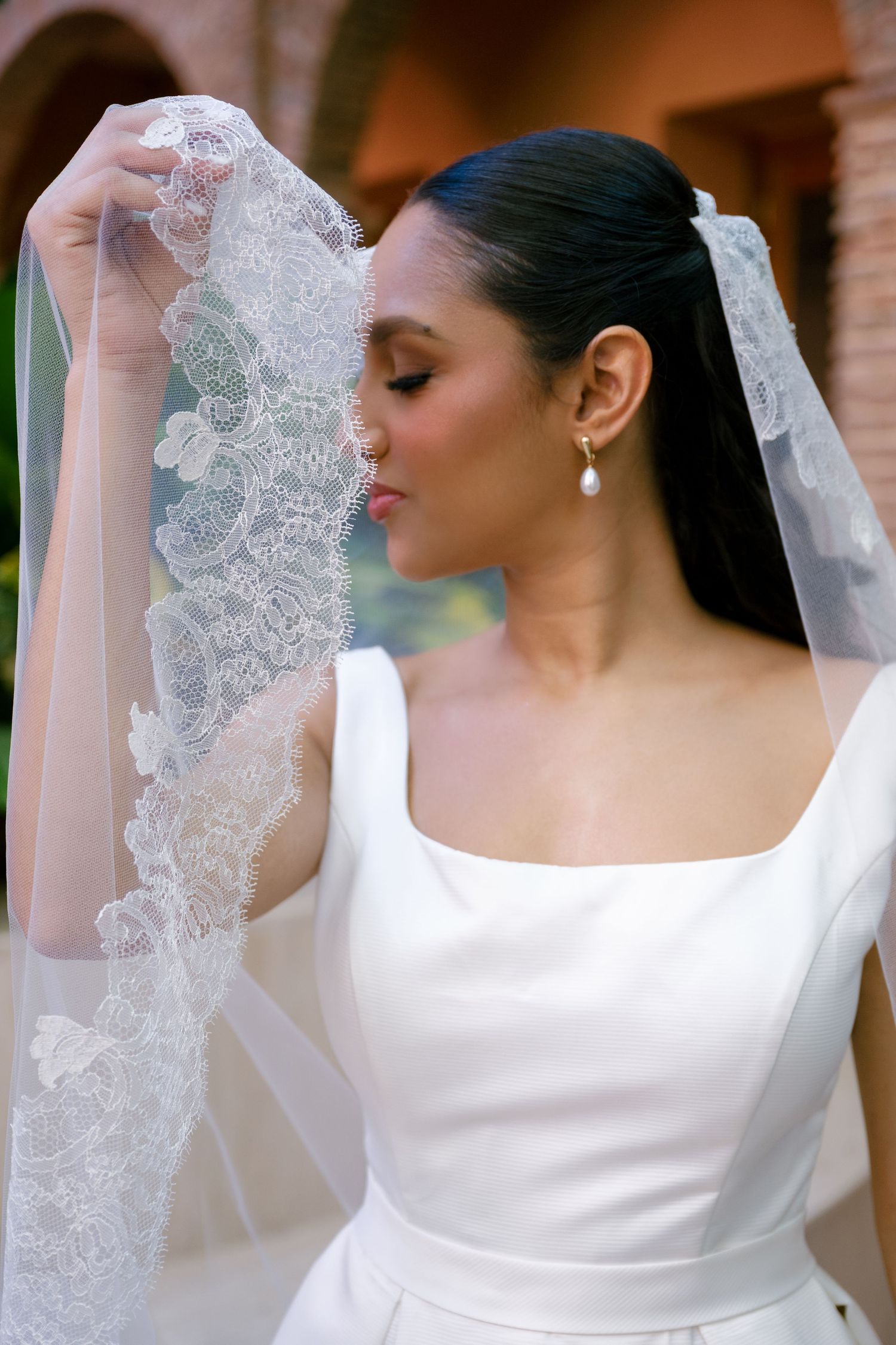 Close-up details of delicate lace veil and classic white wedding dress with boat neckline.