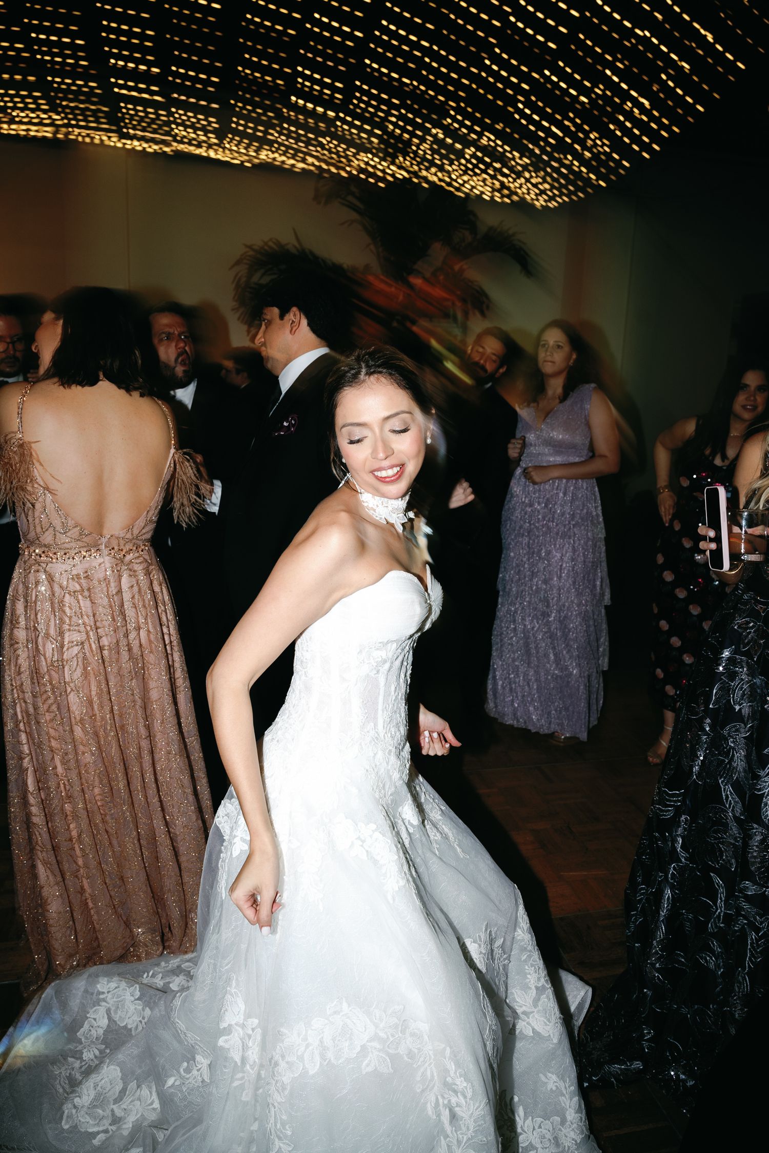 Wedding guests dancing under twinkling string lights at an evening reception celebration.