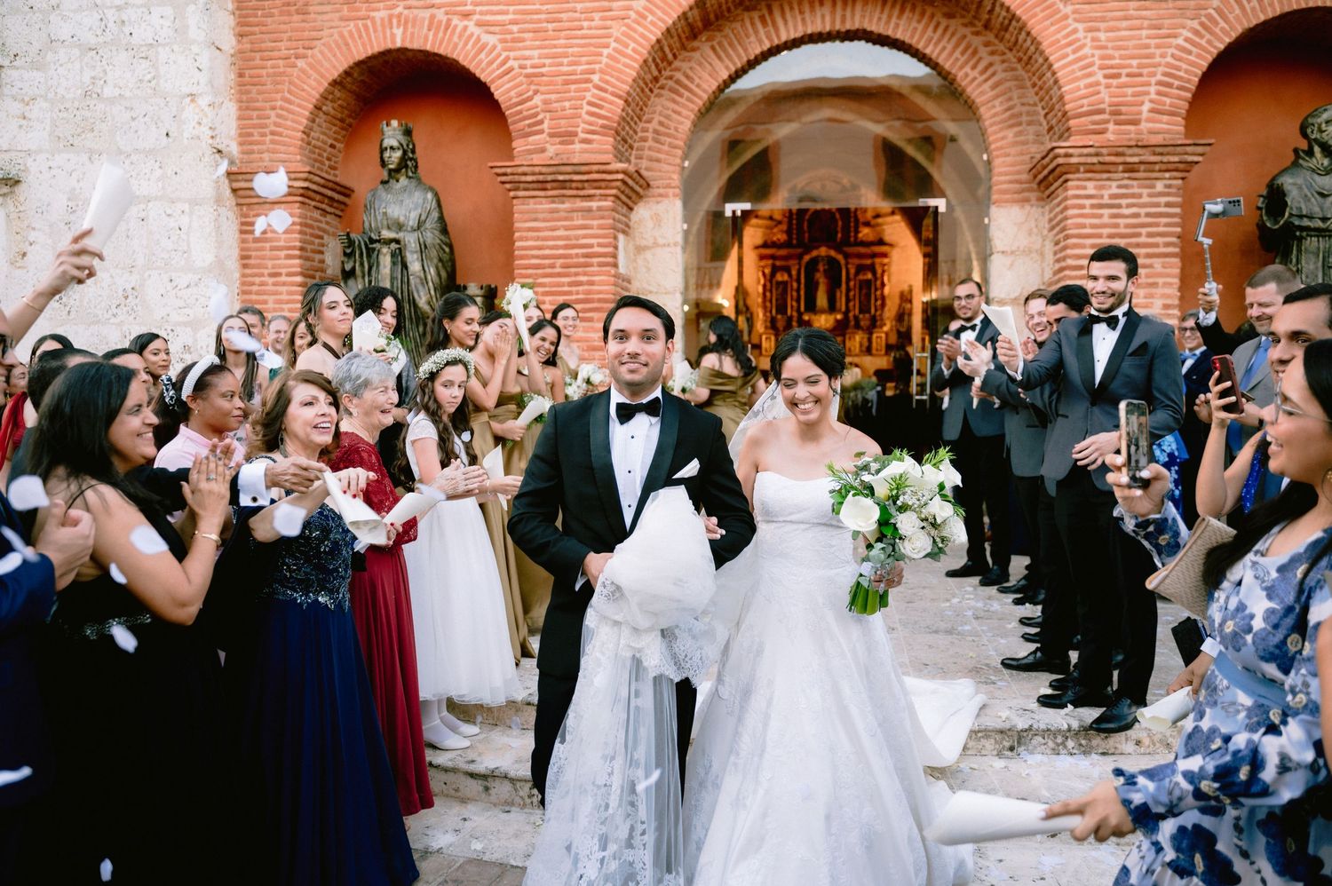 Wedding guests dance and celebrate during an evening reception in an elegant brick-arched venue.