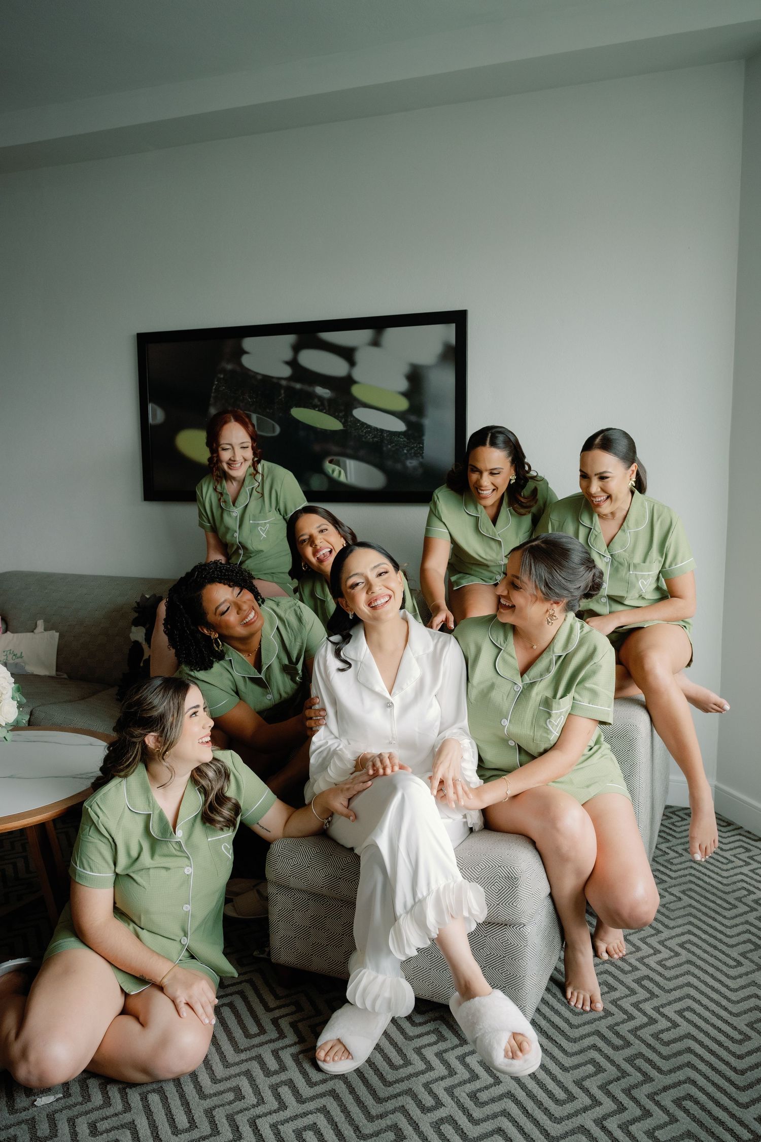 A group in matching sage green outfits share candid moments and laughter during a wedding preparation photoshoot.