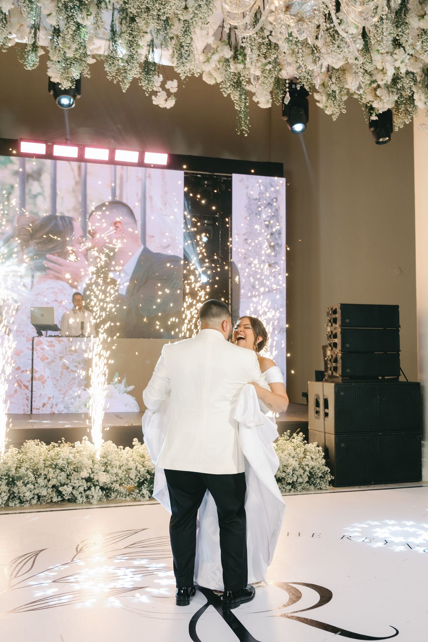 Newlyweds dance together under hanging floral arrangements and sparkling lights at their reception.