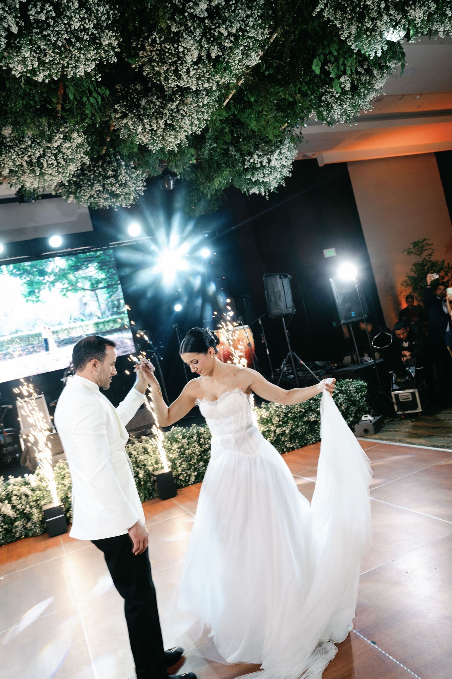 Couple performs their first dance as newlyweds under dramatic lighting and floral decorations.