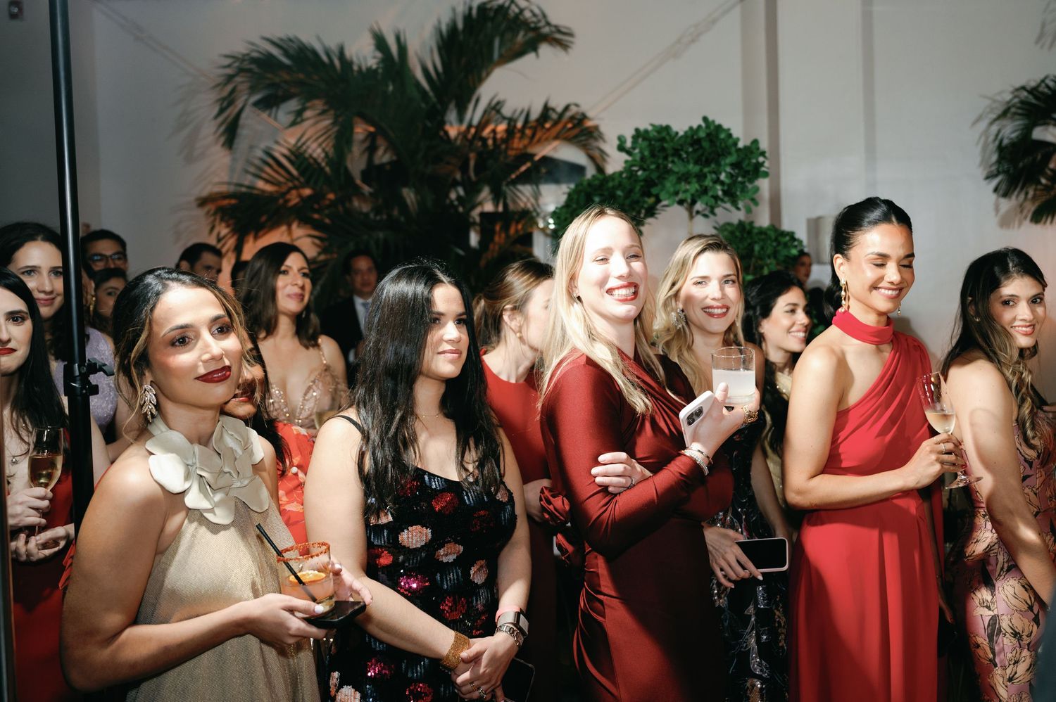 Large group of wedding guests in red dresses socializing at an elegant reception event.