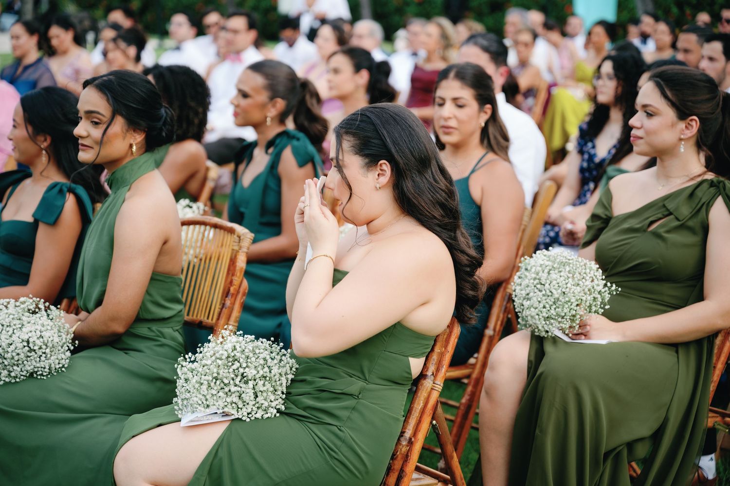 Wedding guests in emerald green dresses seated in rows at an outdoor ceremony.