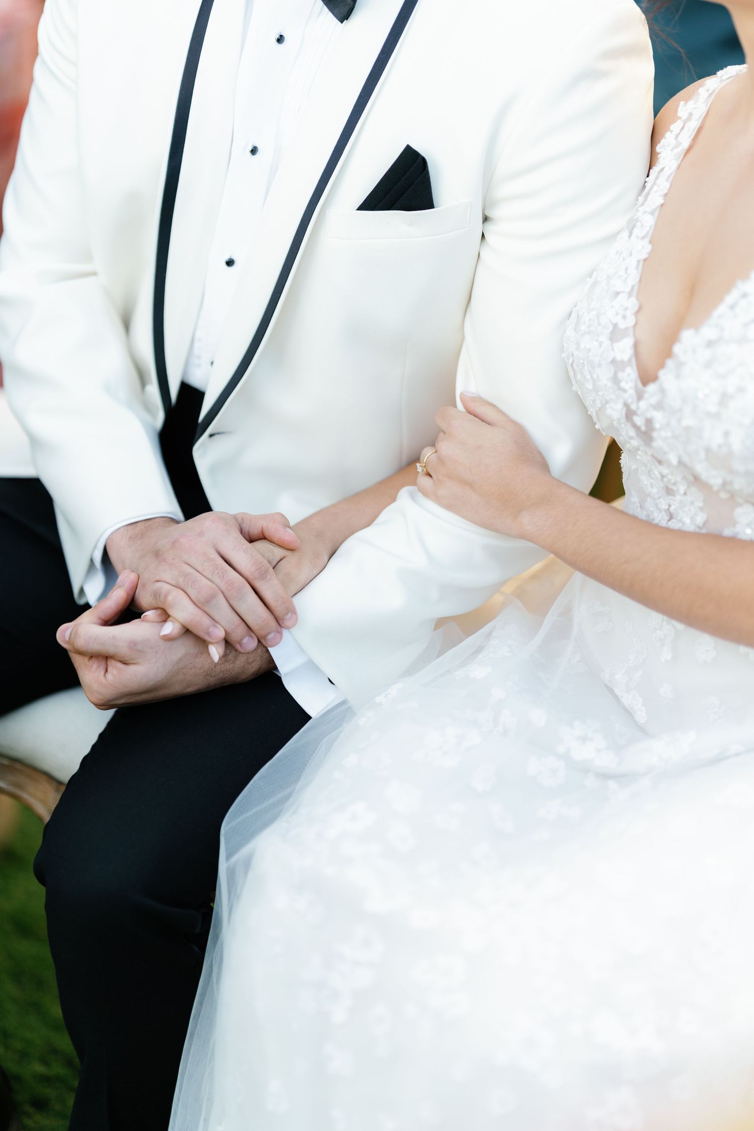 A bride and groom hold hands while wearing formal wedding attire in white and black.