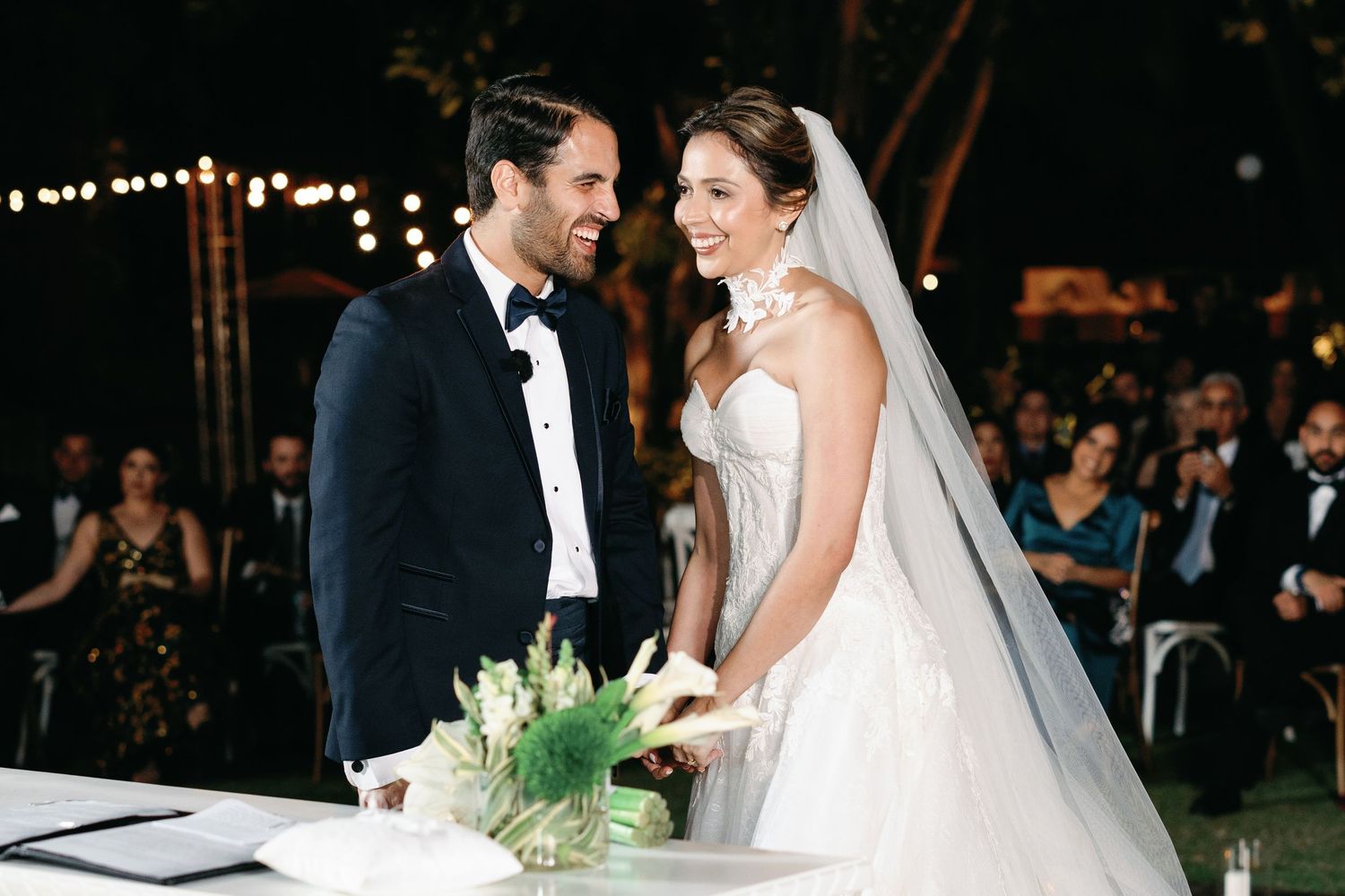 Couple shares a joyful moment during their nighttime wedding ceremony under twinkling lights.