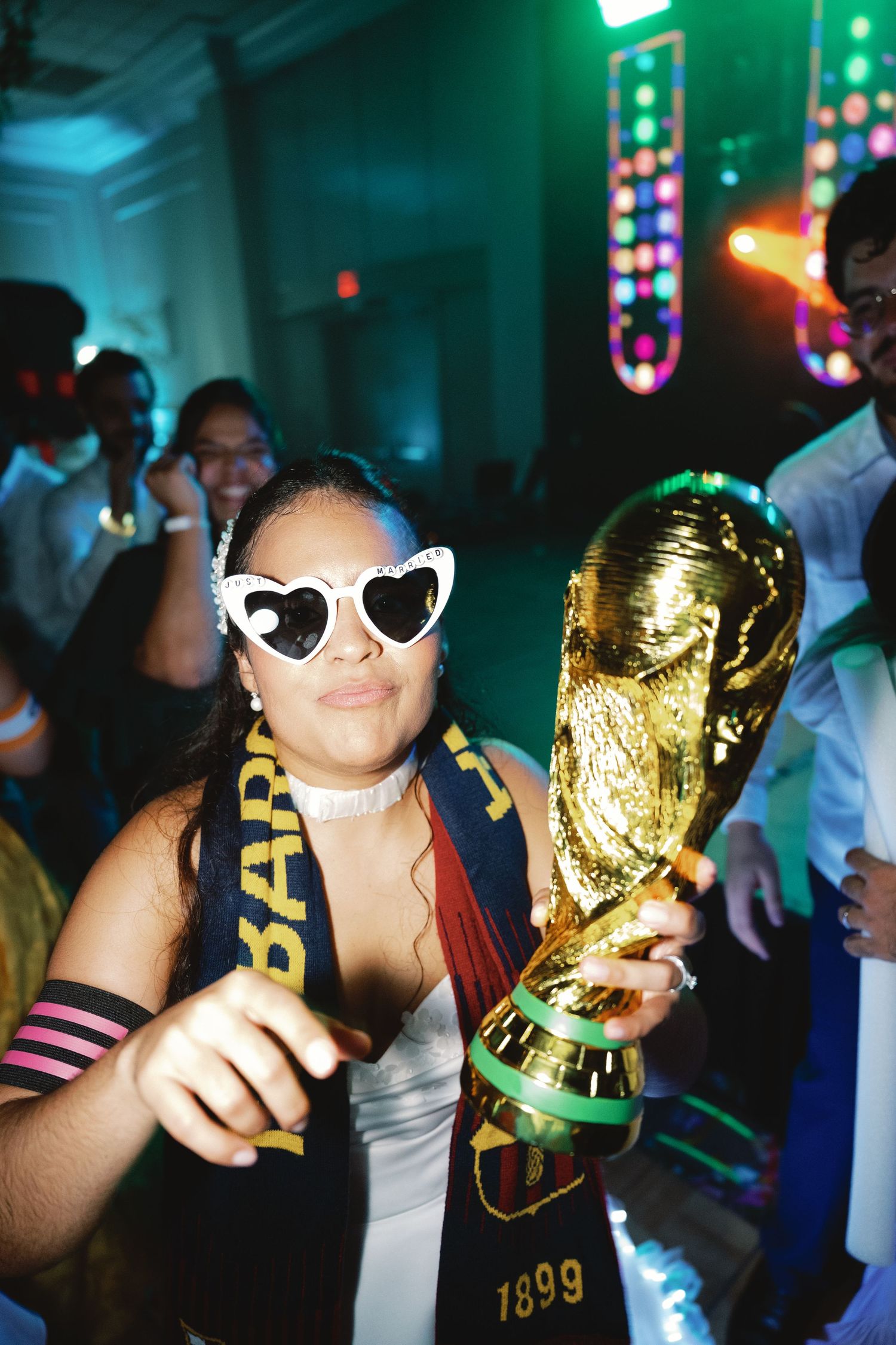 A golden World Cup trophy being held up at a party with colorful lights in the background.