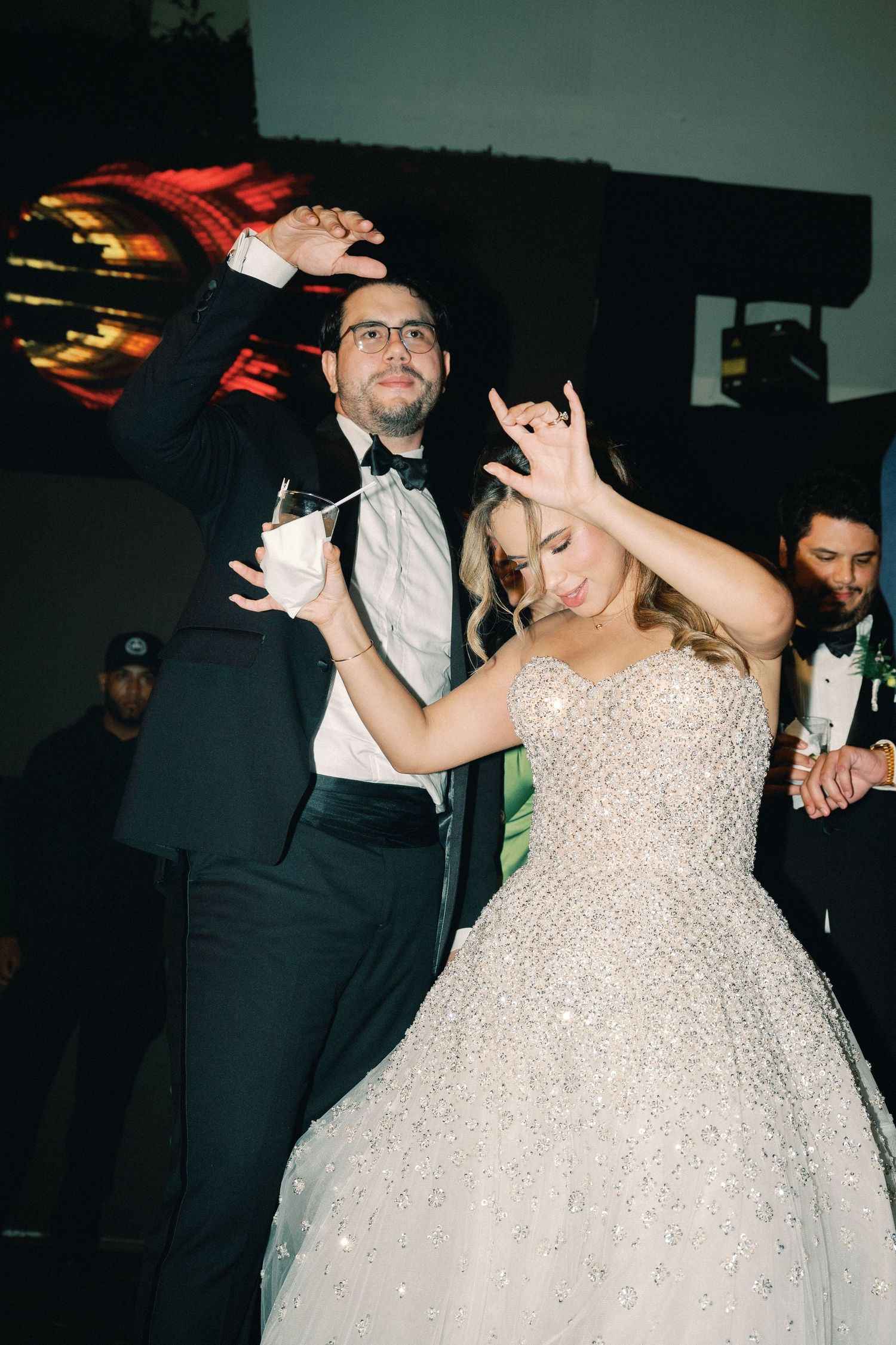 Wedding couple dancing energetically at their reception as they hold drinks and celebrate on the dance floor.