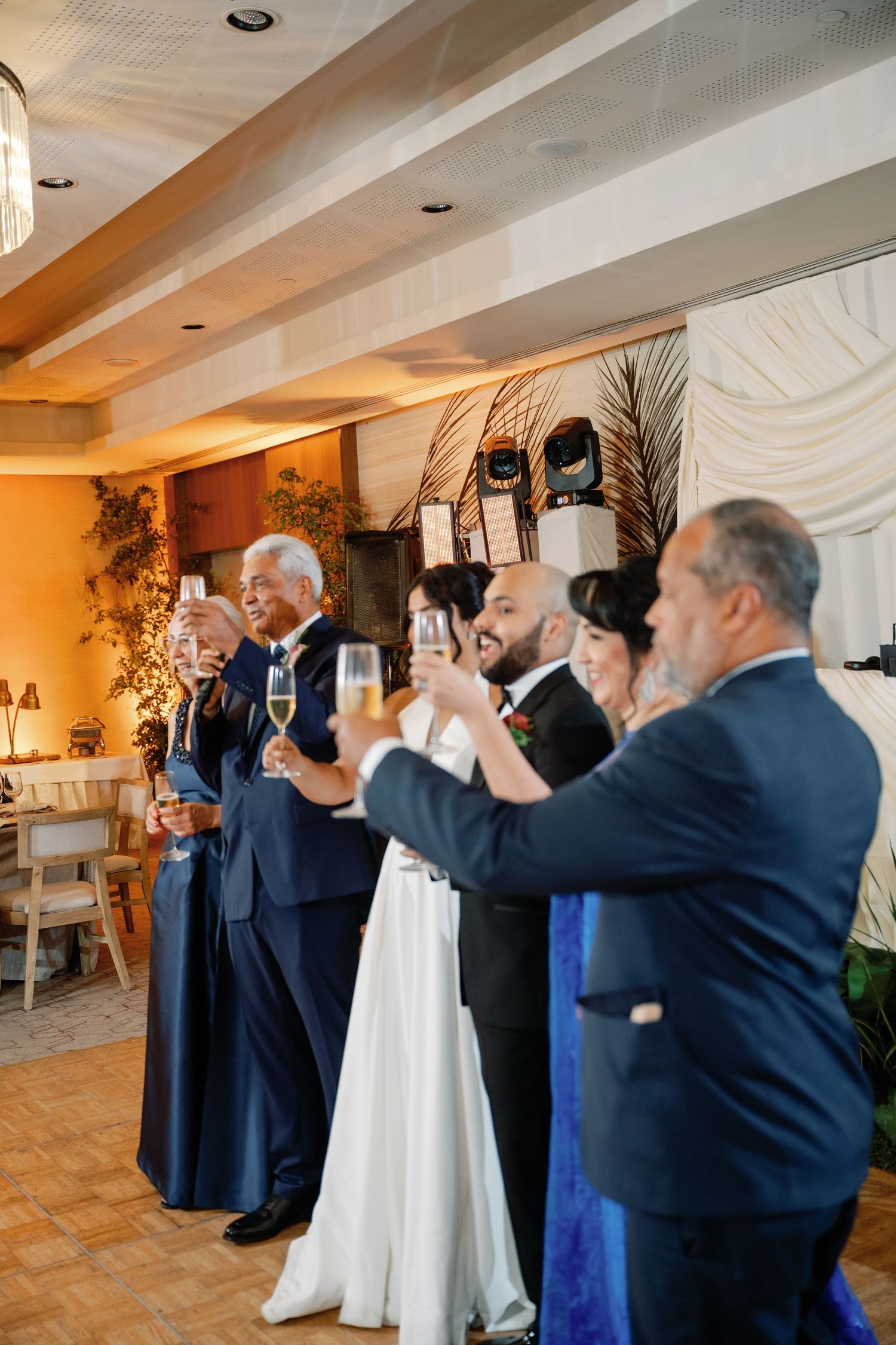 Wedding guests raise champagne glasses in a toast during an elegant indoor reception celebration.