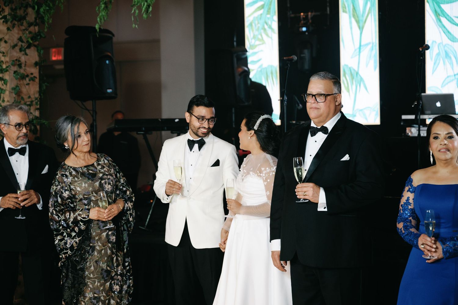 Elegant wedding guests in formal attire gather for cocktails at an evening reception with decorative wall panels.