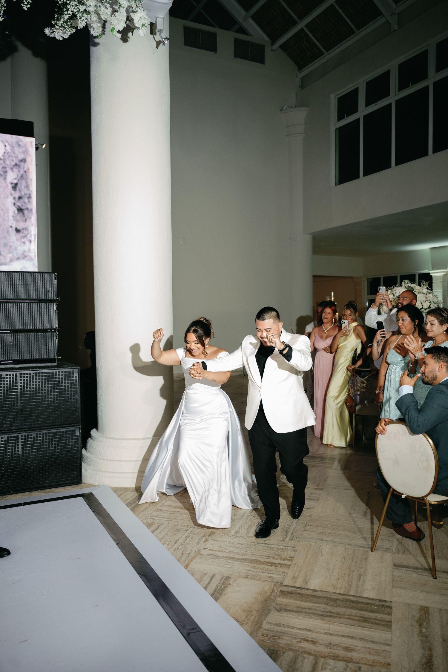Wedding party performing choreographed dance routine in elegant white venue with columns.