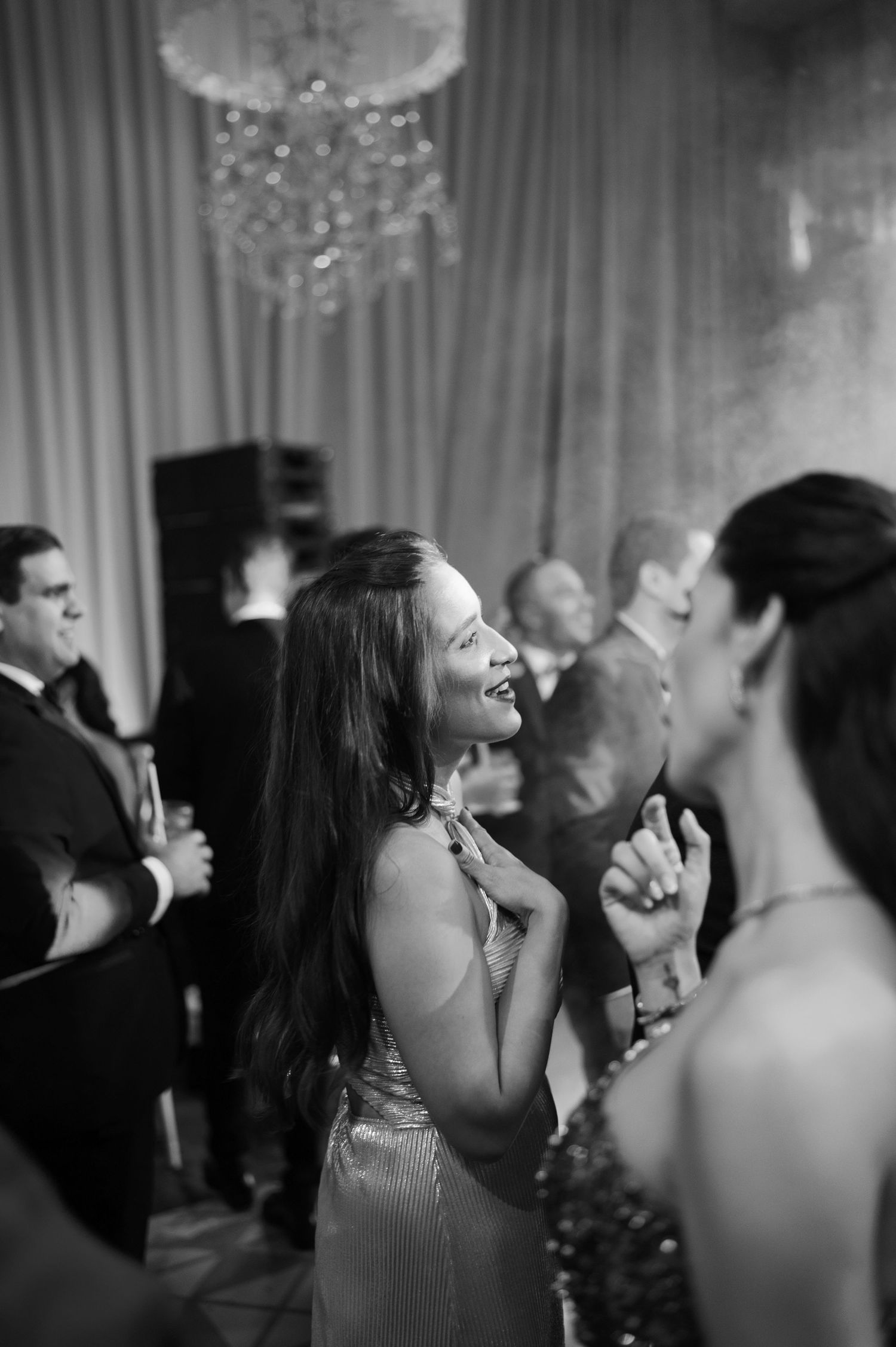 Guests dancing and celebrating at a formal party with elegant drapes and lighting visible in the background.