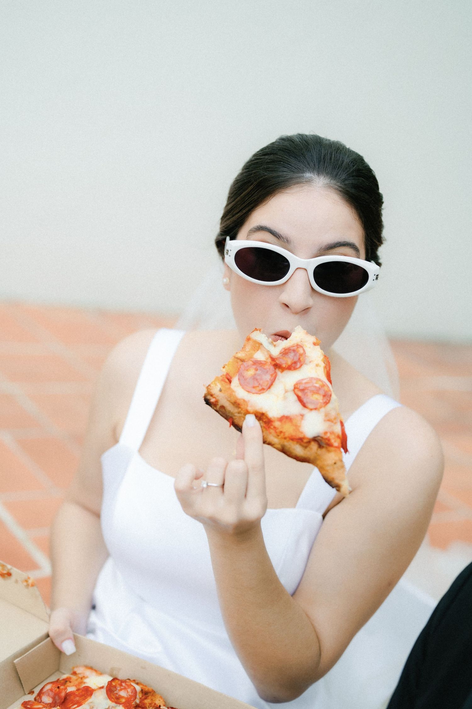 Someone wearing white sunglasses and a white top takes bites of pizza in a sequence of four connected photos.