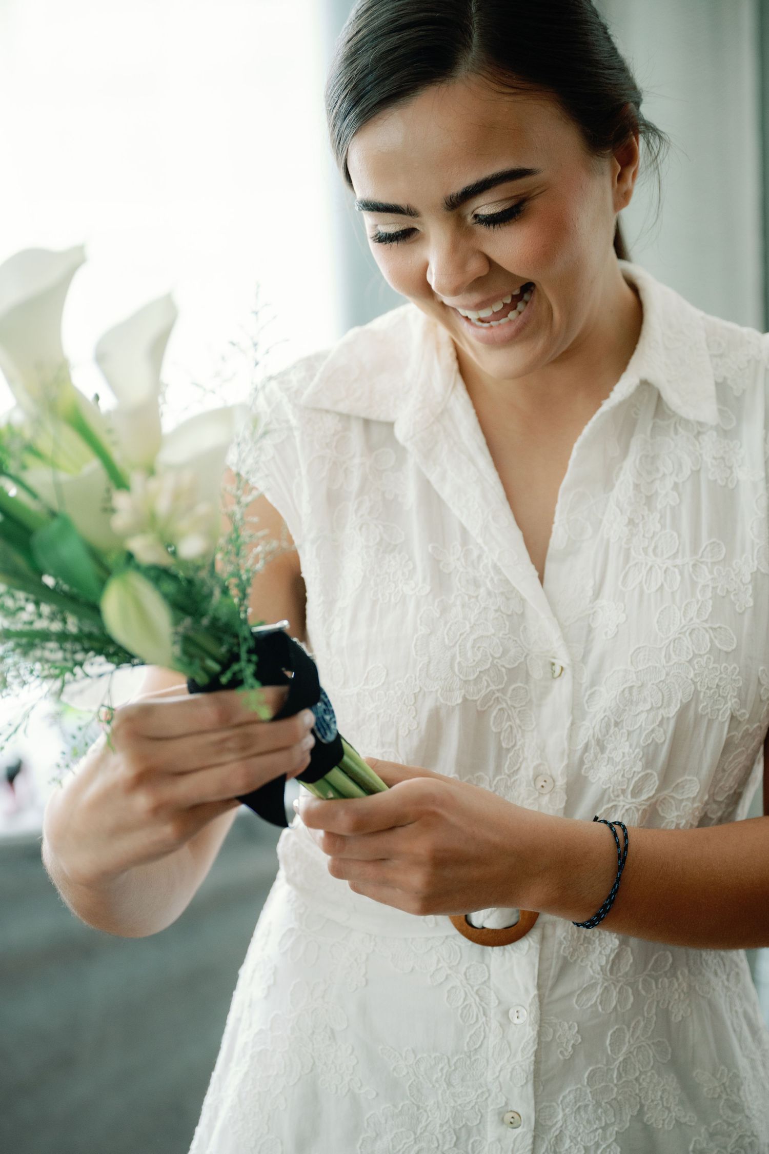 Someone wearing a white lace blouse smiles while arranging white lilies and greenery in a floral arrangement.